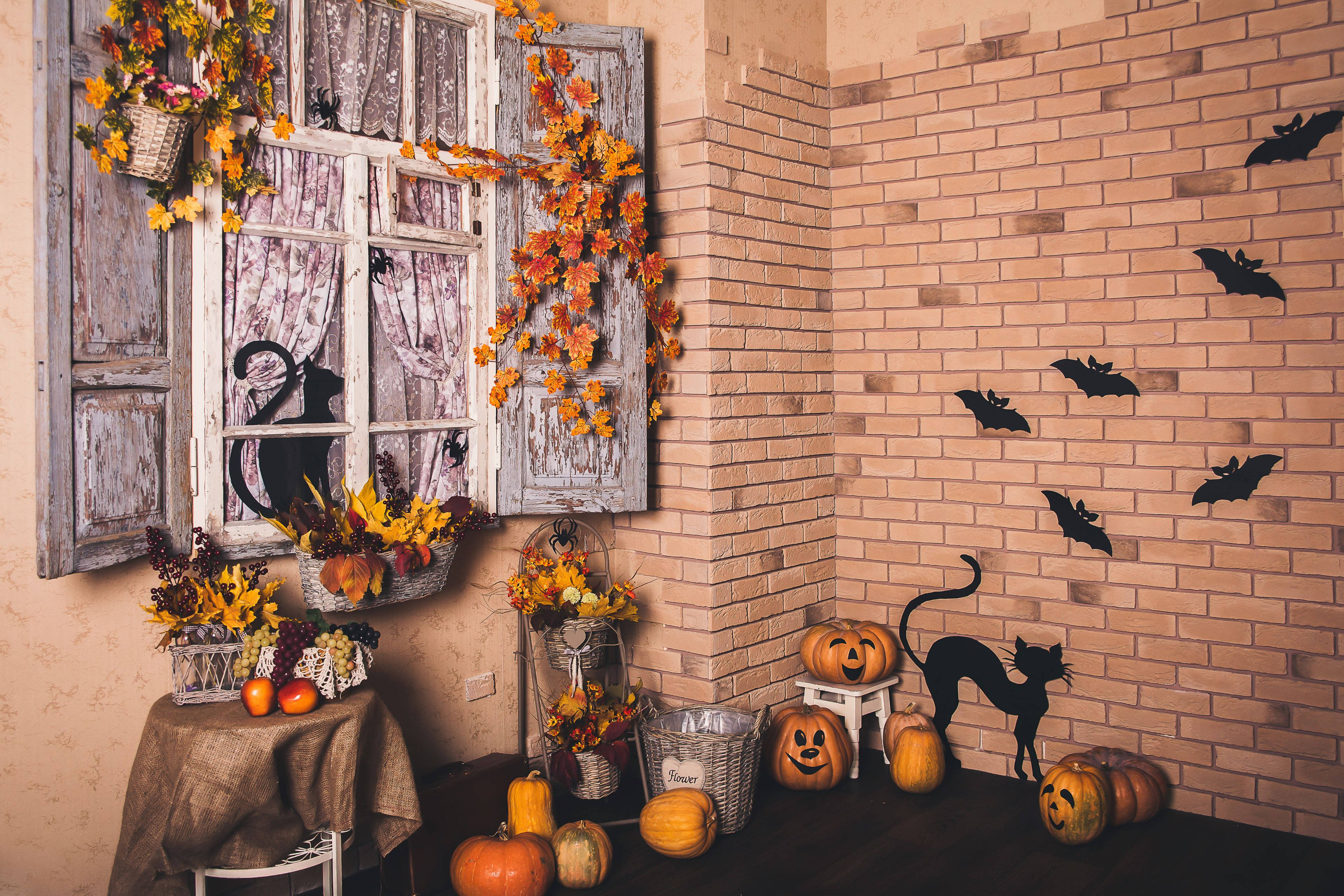 Halloween Aesthetic 桌布 壁紙 — 一個舒適的萬聖節角落，用南瓜、蝙蝠和秋葉裝飾磚牆和鄉村風格的窗戶。