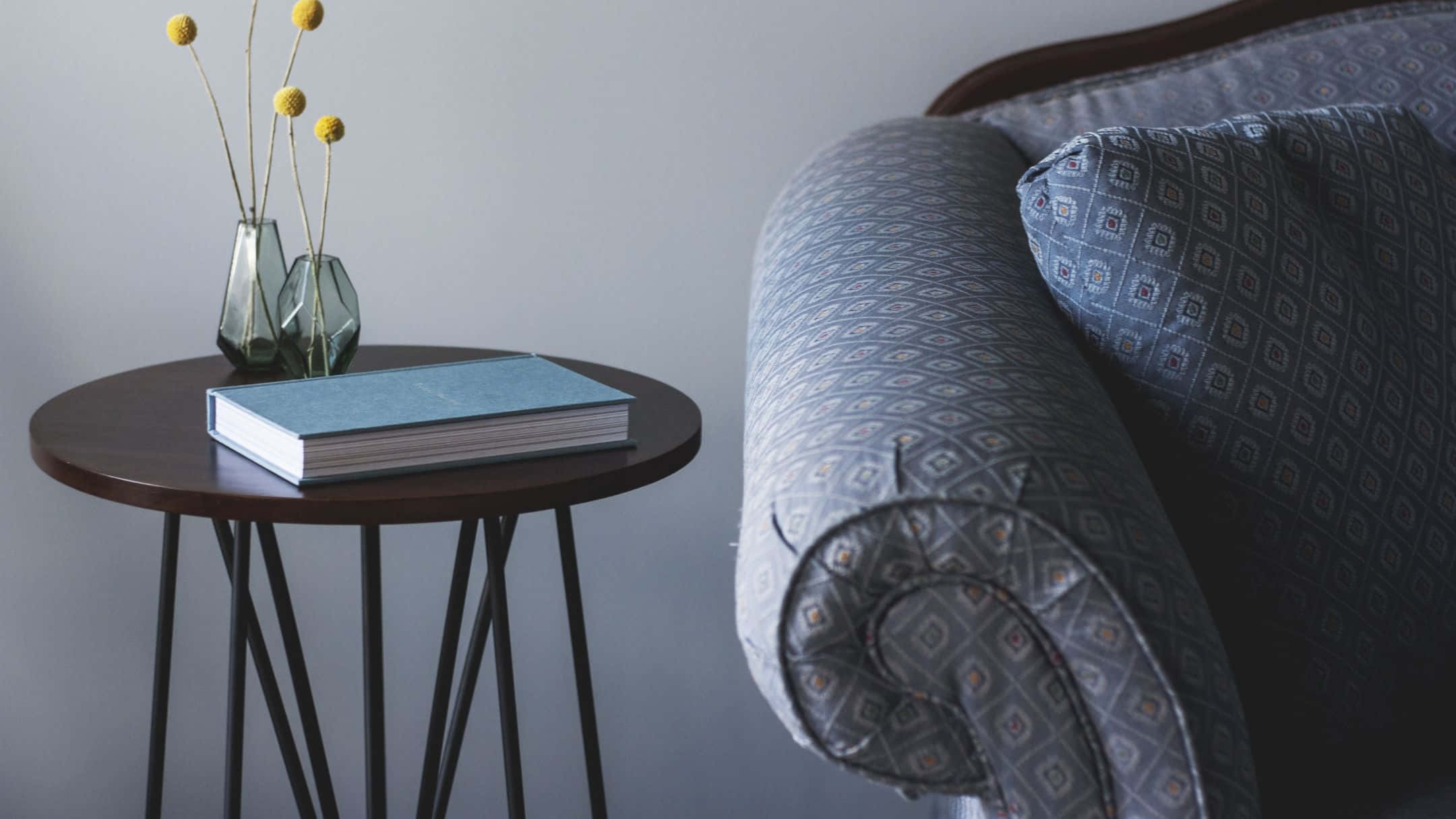 Furniture 桌布 壁紙 — 一個舒適的角落，有一張圖案扶手椅，旁邊是一張木製邊桌，上面放著一本書和兩個裝有黃色花朵的玻璃花瓶。