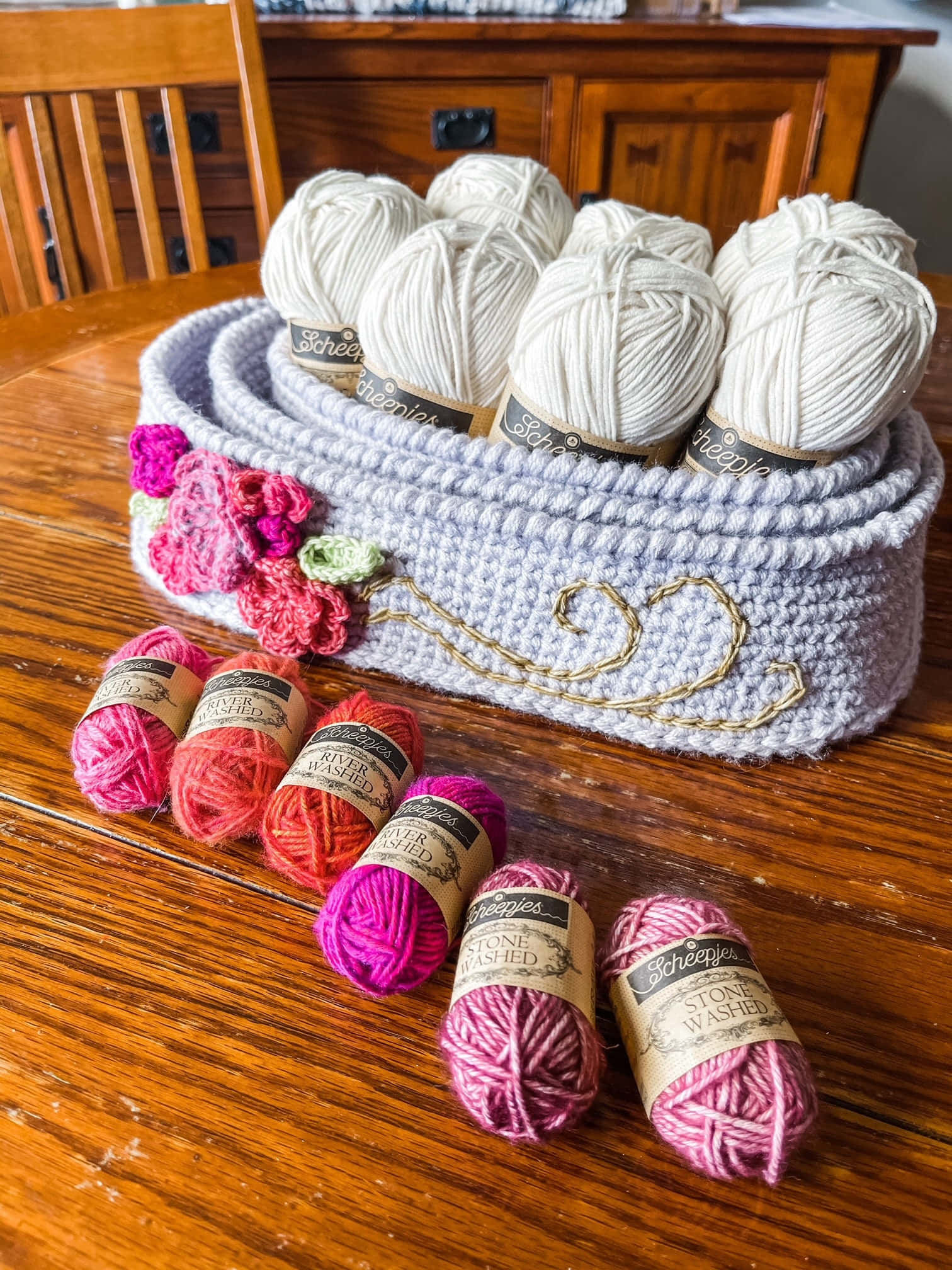 Crochet 桌布 壁紙 — 一個舒適的鉤針編織籃子，裡面裝滿了白色毛線球，放在木桌上，旁邊是充滿活力的粉紅色和紅色毛線束。