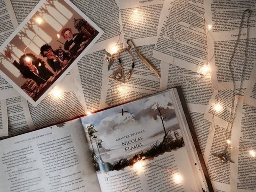 hp aesthetic 桌布 壁紙 — 一個舒適的閱讀角落，有一本名為 Nicolas Flamel 的打開的書，周圍環繞著仙女燈和復古照片，放在報紙頁面上。