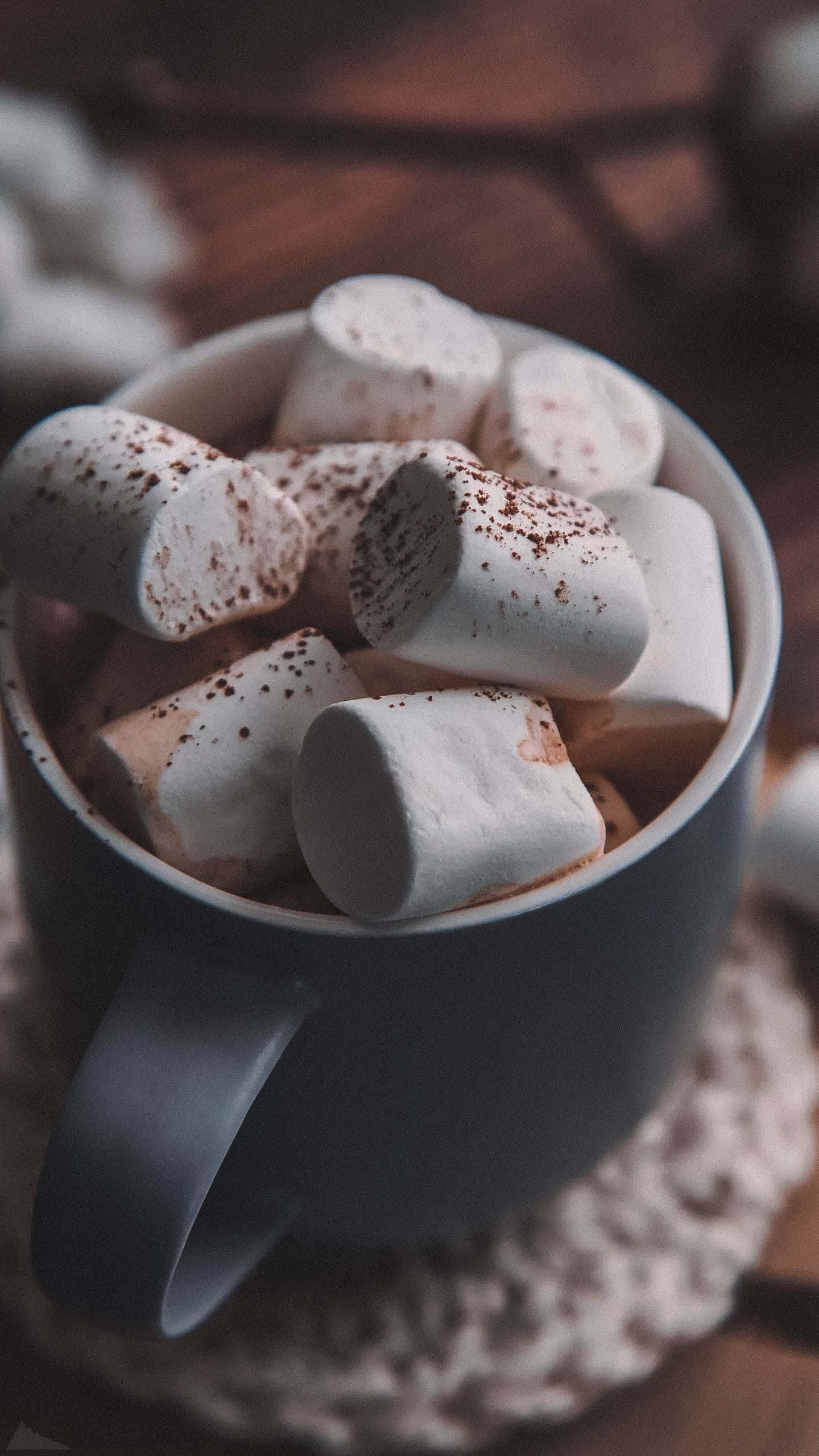 Hot Chocolate 桌布 壁紙 — 一個舒適的馬克杯裝滿融化的棉花糖和可可粉，放在編織杯墊上。