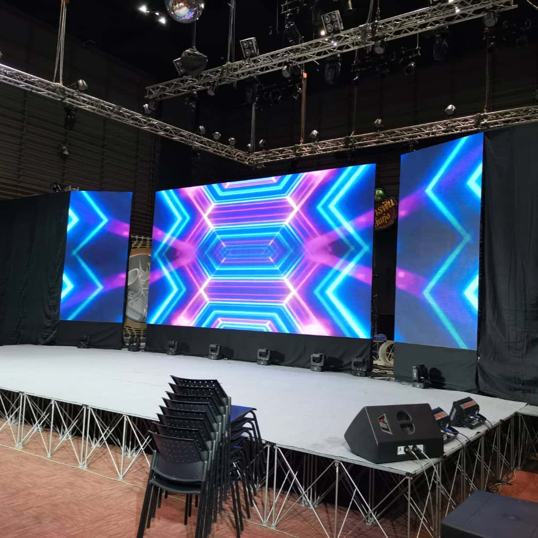 Stage 桌布 壁紙 — 一個舞台，設有三個大型LED螢幕，在工業照明設備下顯示充滿活力的藍色和紫色幾何圖案。