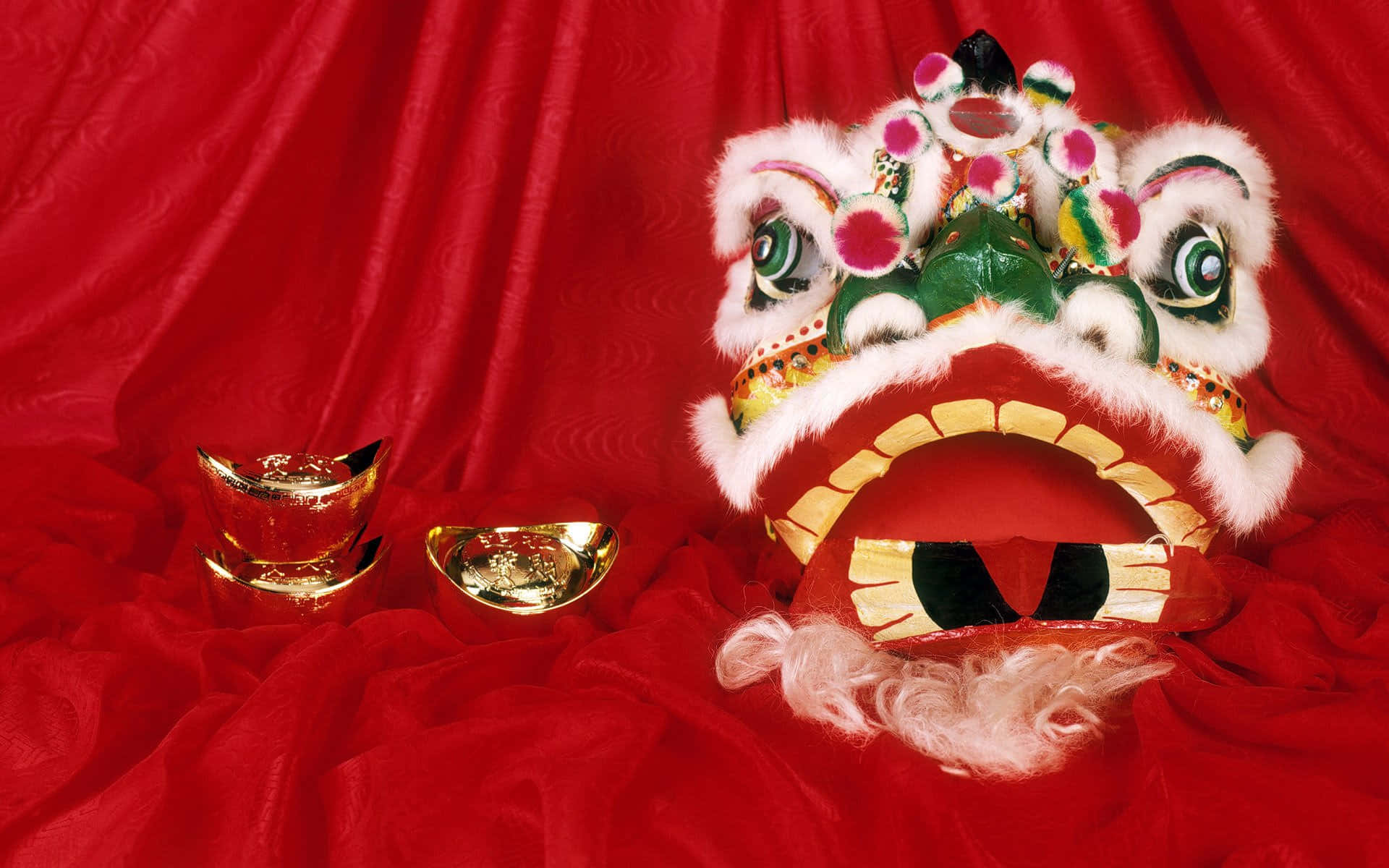 春節 桌布 壁紙 — 一個色彩繽紛、眼睛鮮豔的中國舞獅頭，搭配金元寶，放置在濃郁的紅色天鵝絨背景上。