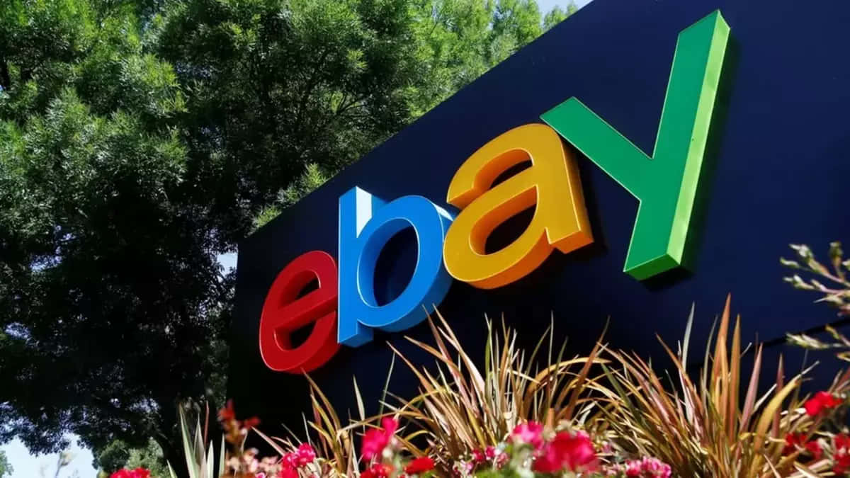 Brand 桌布 壁紙 — 一個色彩繽紛的3D eBay標誌招牌在明亮的日光下，以綠樹和開花植物為背景，矗立在戶外。