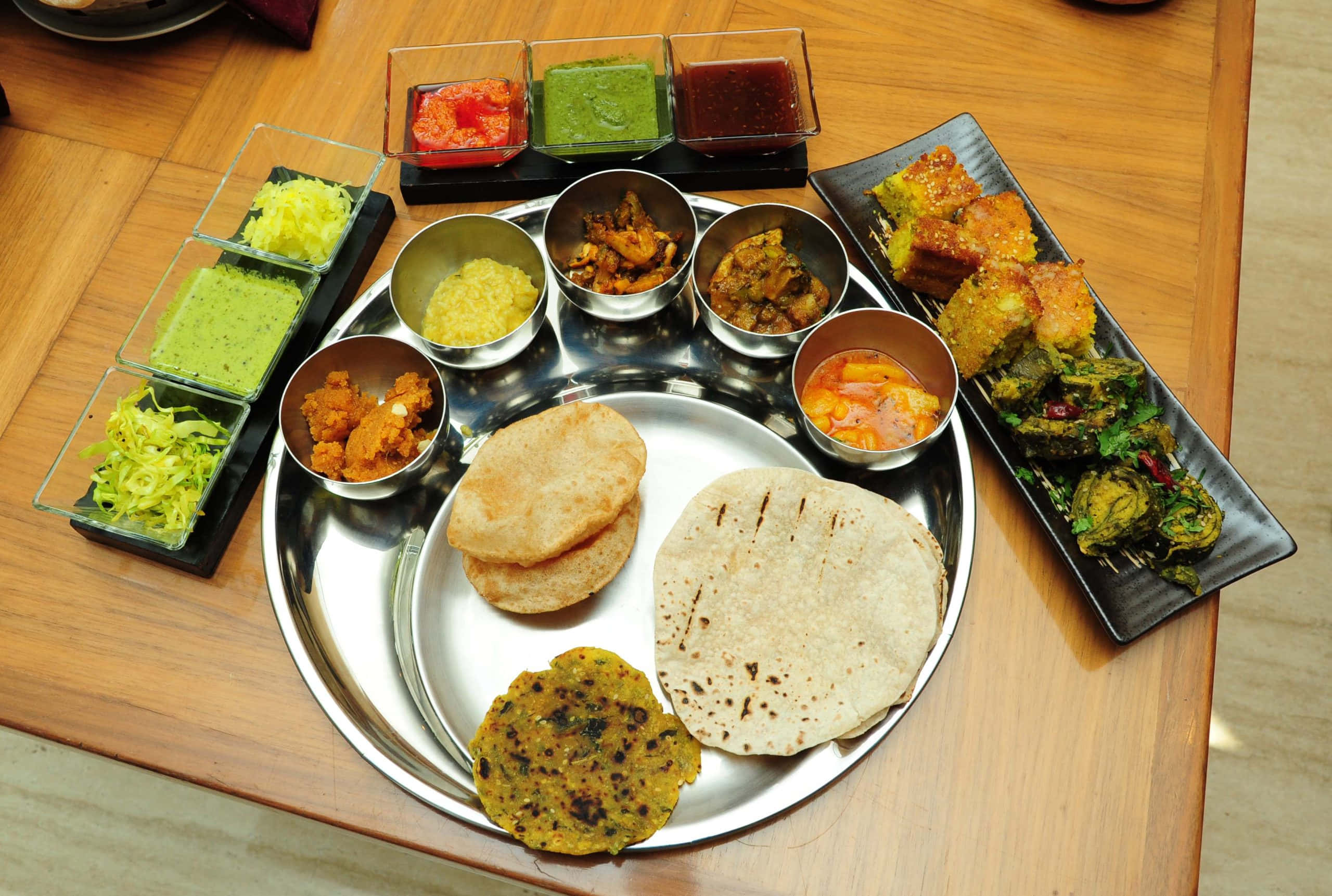Thali 桌布 壁紙 — 一個色彩繽紛的印度塔利餐盤放在銀托盤上，木桌上擺放著烤餅、咖哩、酸辣醬和油炸小吃。