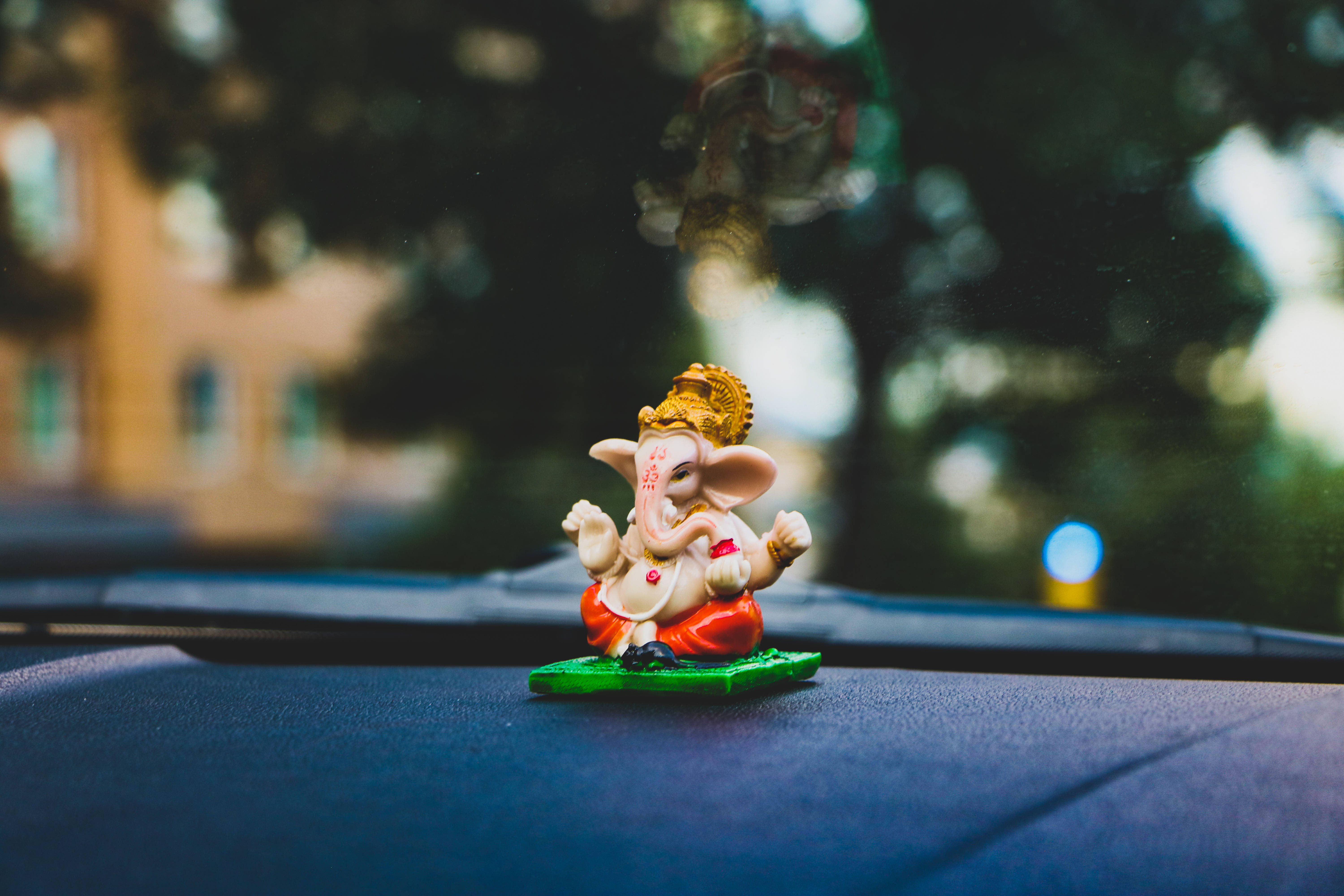 Bappa 桌布 壁紙 — 一個色彩繽紛的小象神雕像放在汽車儀表板上，背景是模糊的戶外景色。