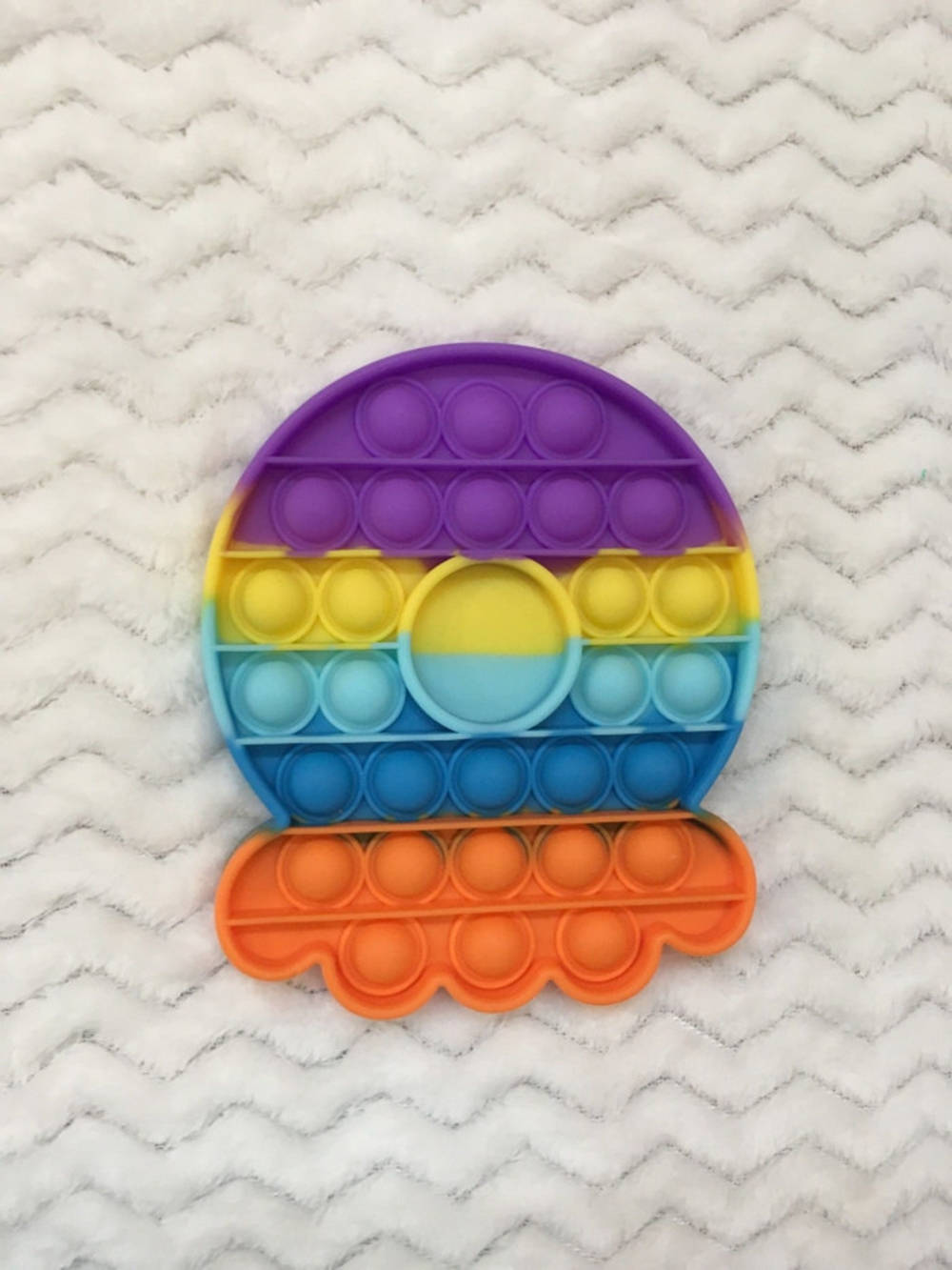 Fidget Toys 桌布 壁紙 — 一個色彩繽紛的彩虹色太陽形狀Pop-it減壓玩具放在一張白色人字形圖案絨毛毯上。