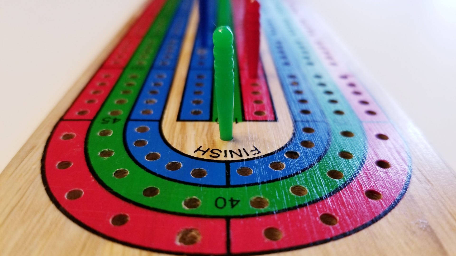 Board Game 桌布 壁紙 — 一個色彩繽紛的木製克里比奇棋盤的特寫，終點線上有綠色棋子。