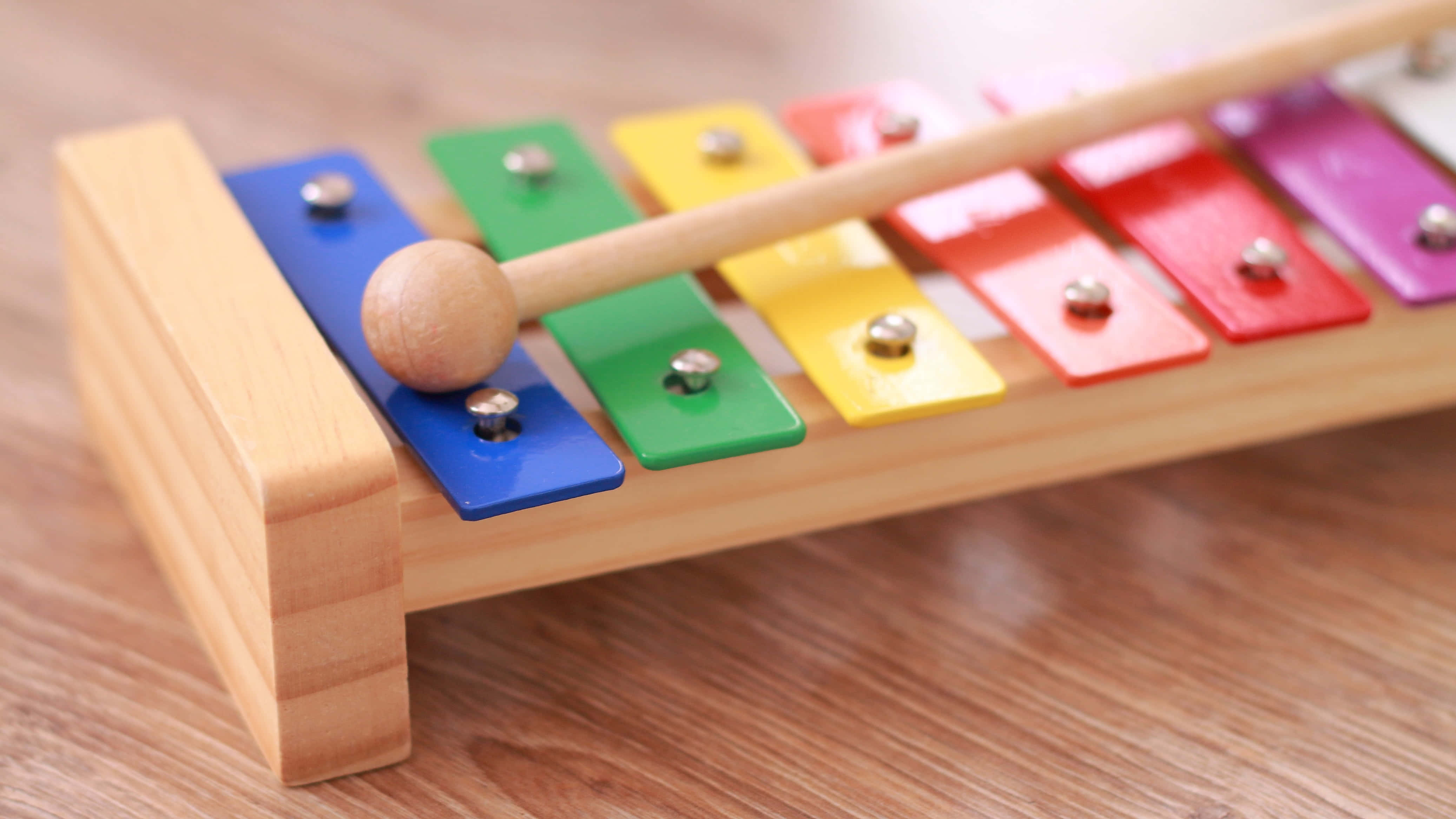 Educational Games 桌布 壁紙 — 一個色彩繽紛的木製木琴特寫，琴鍵呈彩虹色，放置在溫暖的木質表面上。