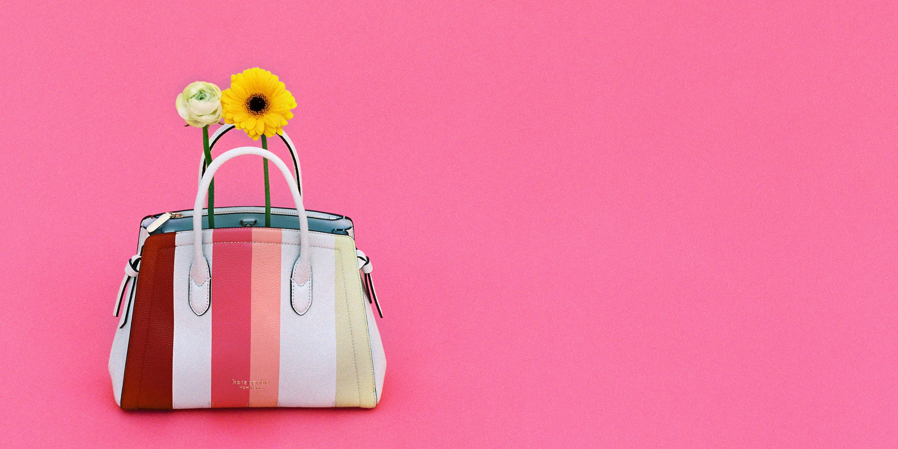 kate spade 桌布 壁紙 — 一個色彩繽紛的條紋手提包，配有白色手柄，在充滿活力的粉紅色背景上放著一朵黃色向日葵和一朵白玫瑰。