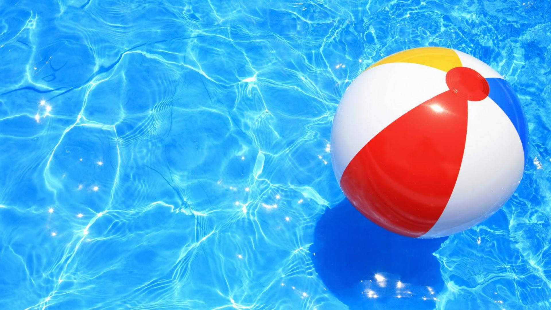 ball 桌布 壁紙 — 一個色彩繽紛的沙灘球漂浮在清澈湛藍的泳池水中，帶有漣漪般的陽光反射。