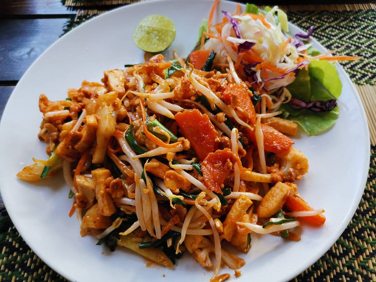 thai 桌布 壁紙 — 一個色彩繽紛的泰式炒河粉，配上豆腐、豆芽、紅蘿蔔和萊姆裝飾，放在編織墊上。