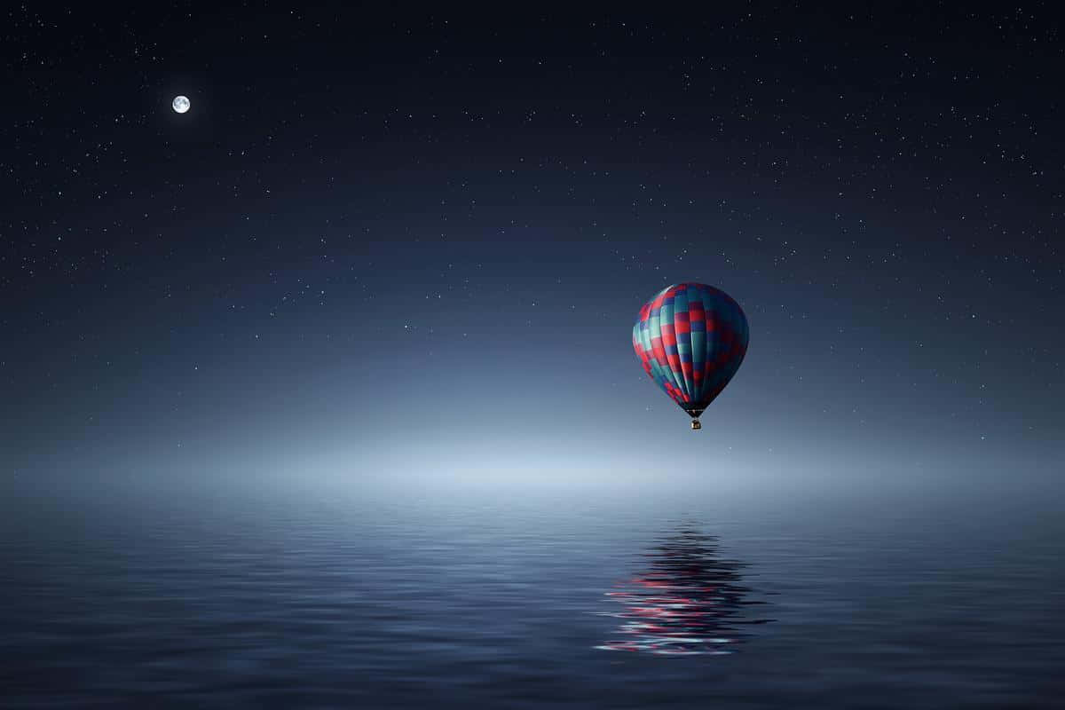 Hot Air Balloon 桌布 壁紙 — 一個色彩繽紛的熱氣球在平靜的水面上空，在可見月亮的星空下寧靜地漂浮。