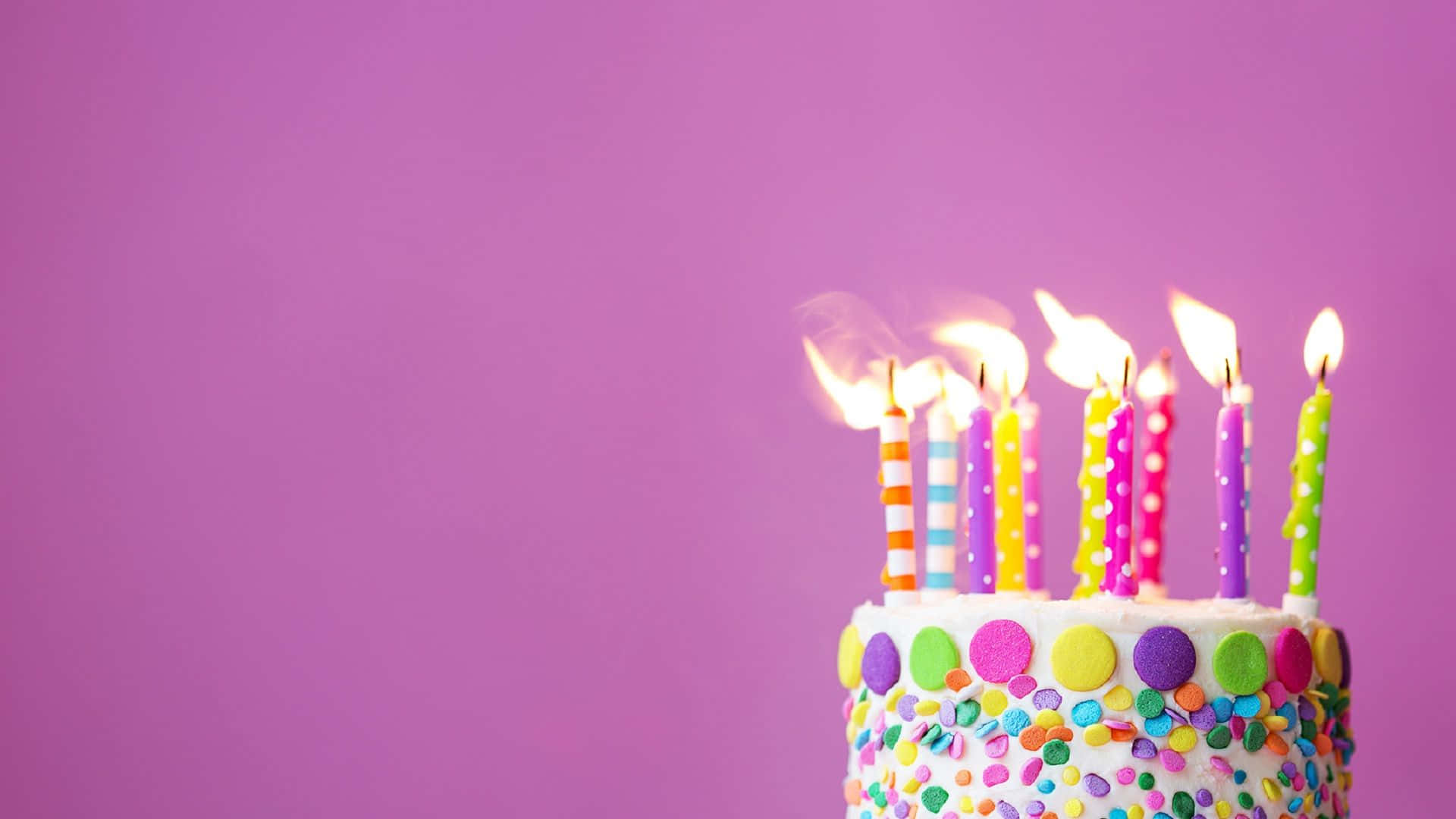 生日快樂 桌布 壁紙 — 一個色彩繽紛的生日蛋糕，上面有燃燒的蠟燭和彩虹糖針，背景為純紫色。