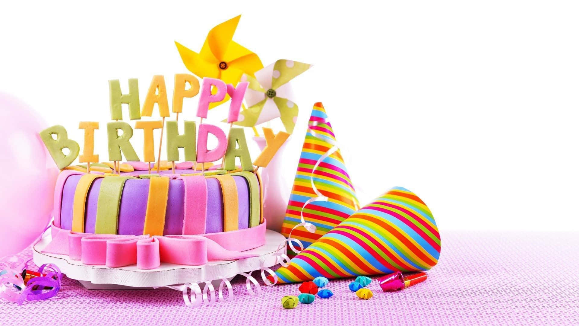 Birthday 桌布 壁紙 — 一個色彩繽紛的生日蛋糕，帶有彩虹條紋絲帶和「生日快樂」字樣，頂部裝飾風車，旁邊有派對帽和氣球，放在粉紅色表面上。
