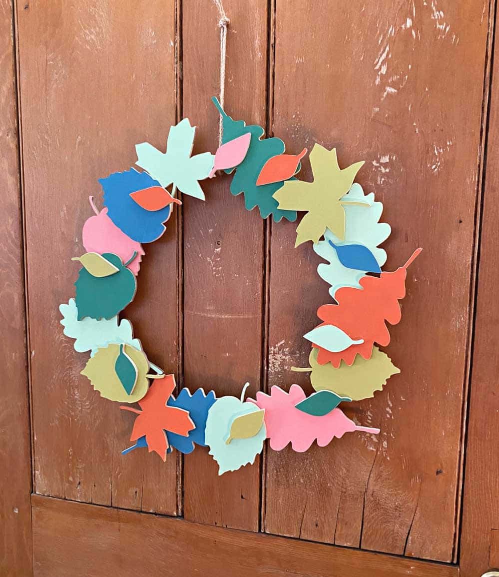 Fall Wreath 桌布 壁紙 — 一個色彩繽紛的紙葉花環掛在帶有明顯木紋和風化質感的鄉村風格木門上。