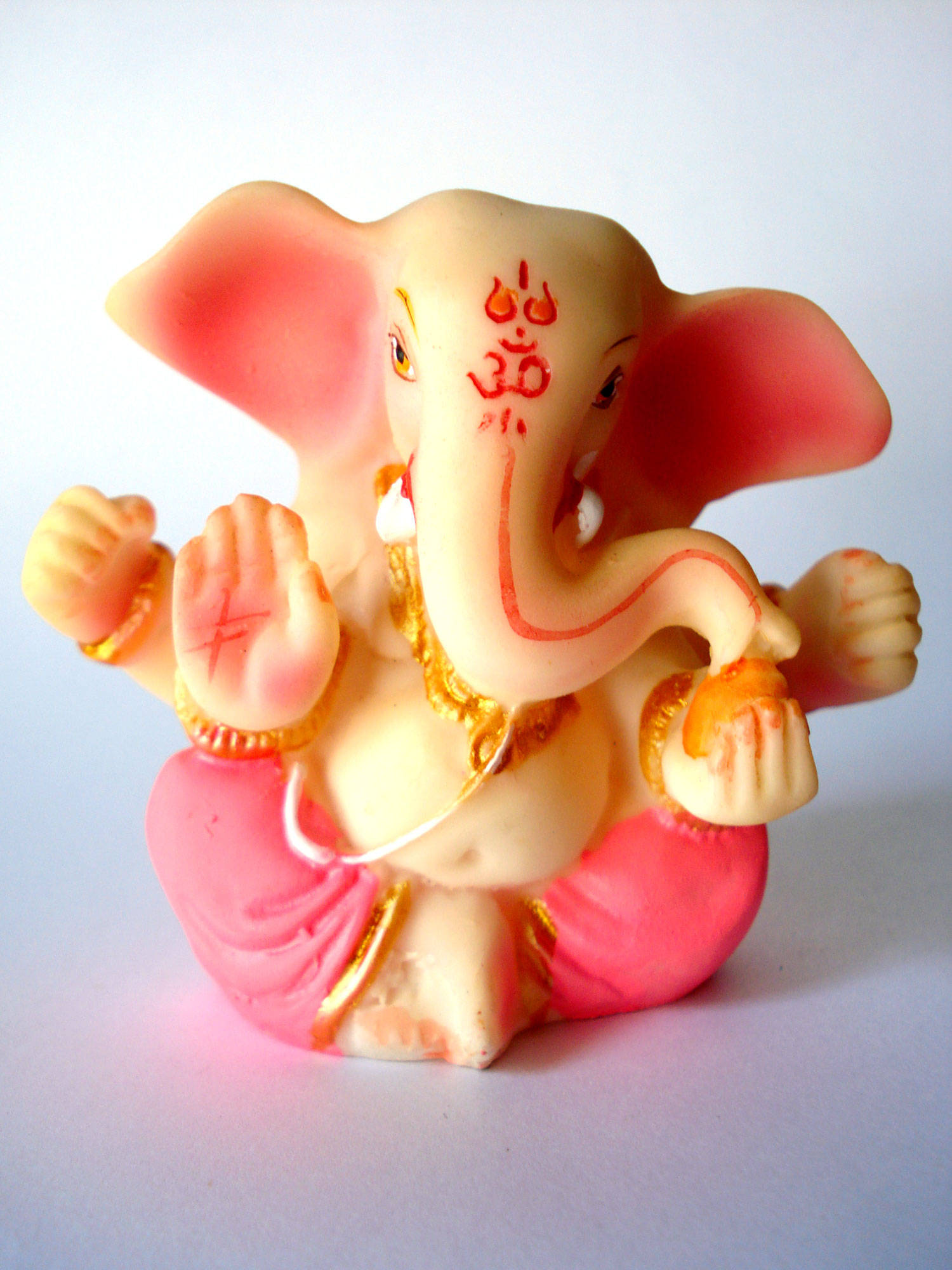 cute ganesha 桌布 壁紙 — 一個色彩繽紛的象神甘尼許塑像，有粉紅色耳朵和金色點綴，放在純白色背景前。