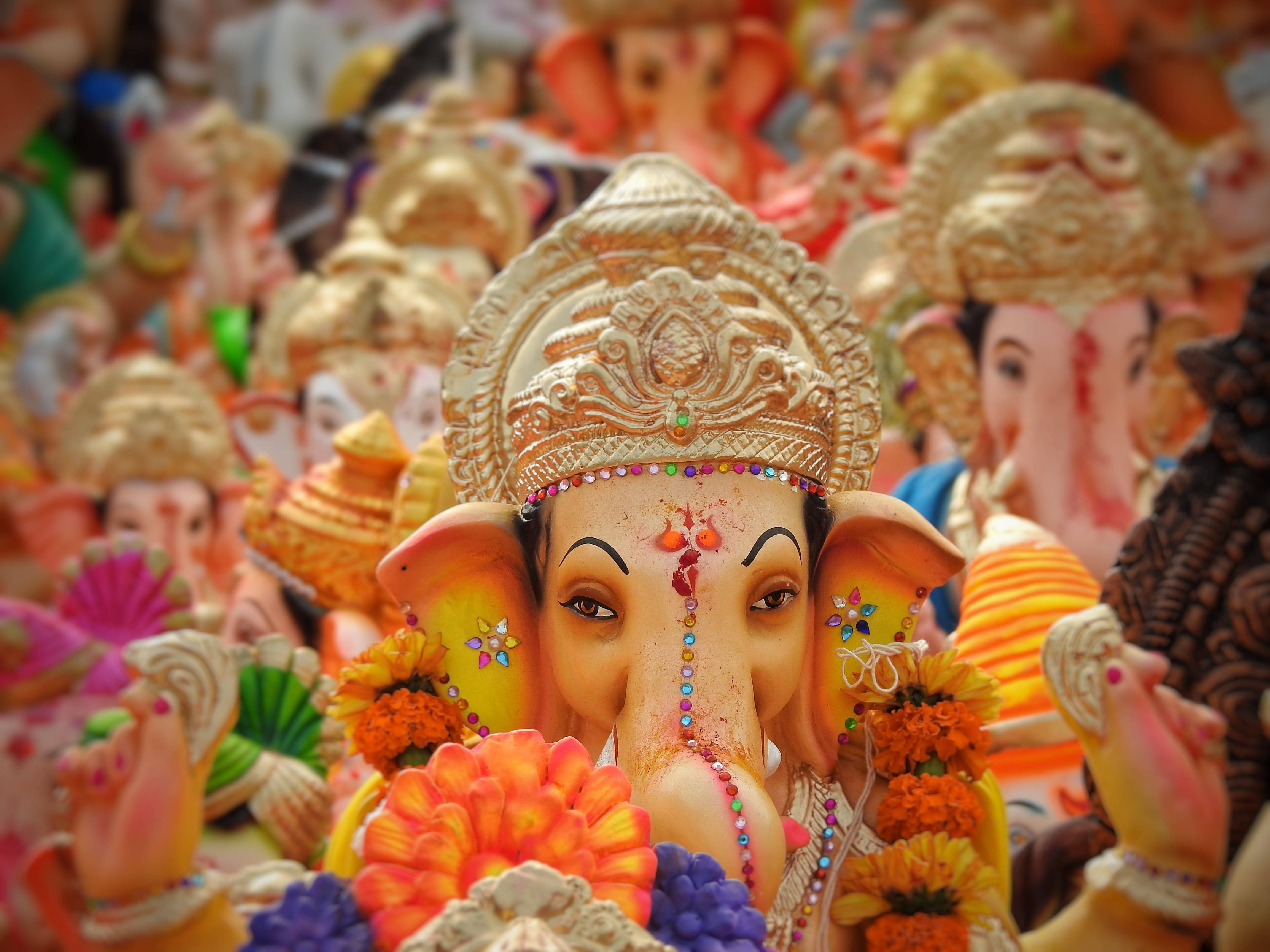 Ganesh 桌布 壁紙 — 一個色彩繽紛的象神雕像特寫，飾有鮮花和珠子，周圍環繞著類似節日偶像的海洋。
