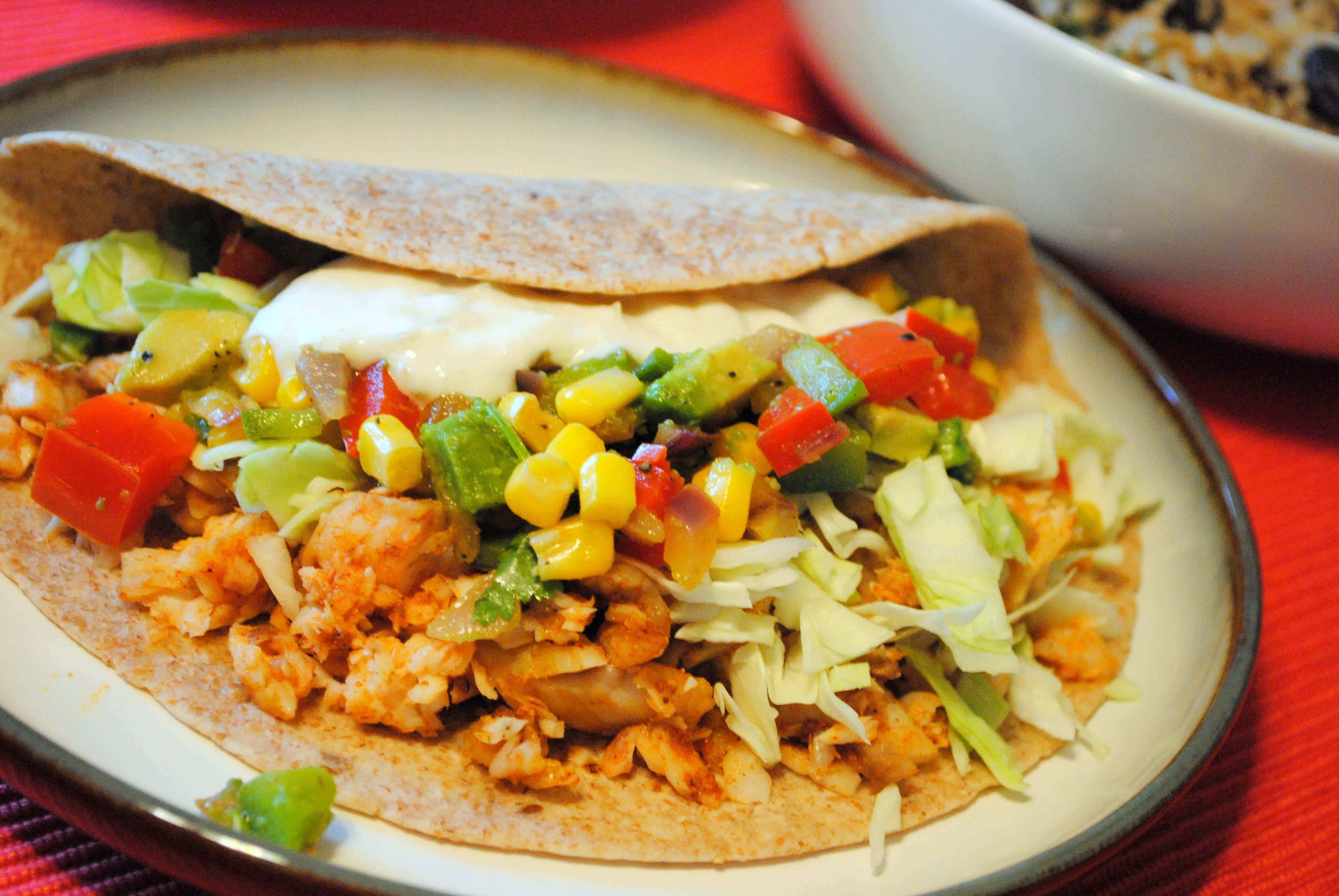 Taco 桌布 壁紙 — 一個色彩繽紛的雞肉墨西哥捲特寫，上面放有玉米、酪梨和酸奶油，盛載在盤子上。