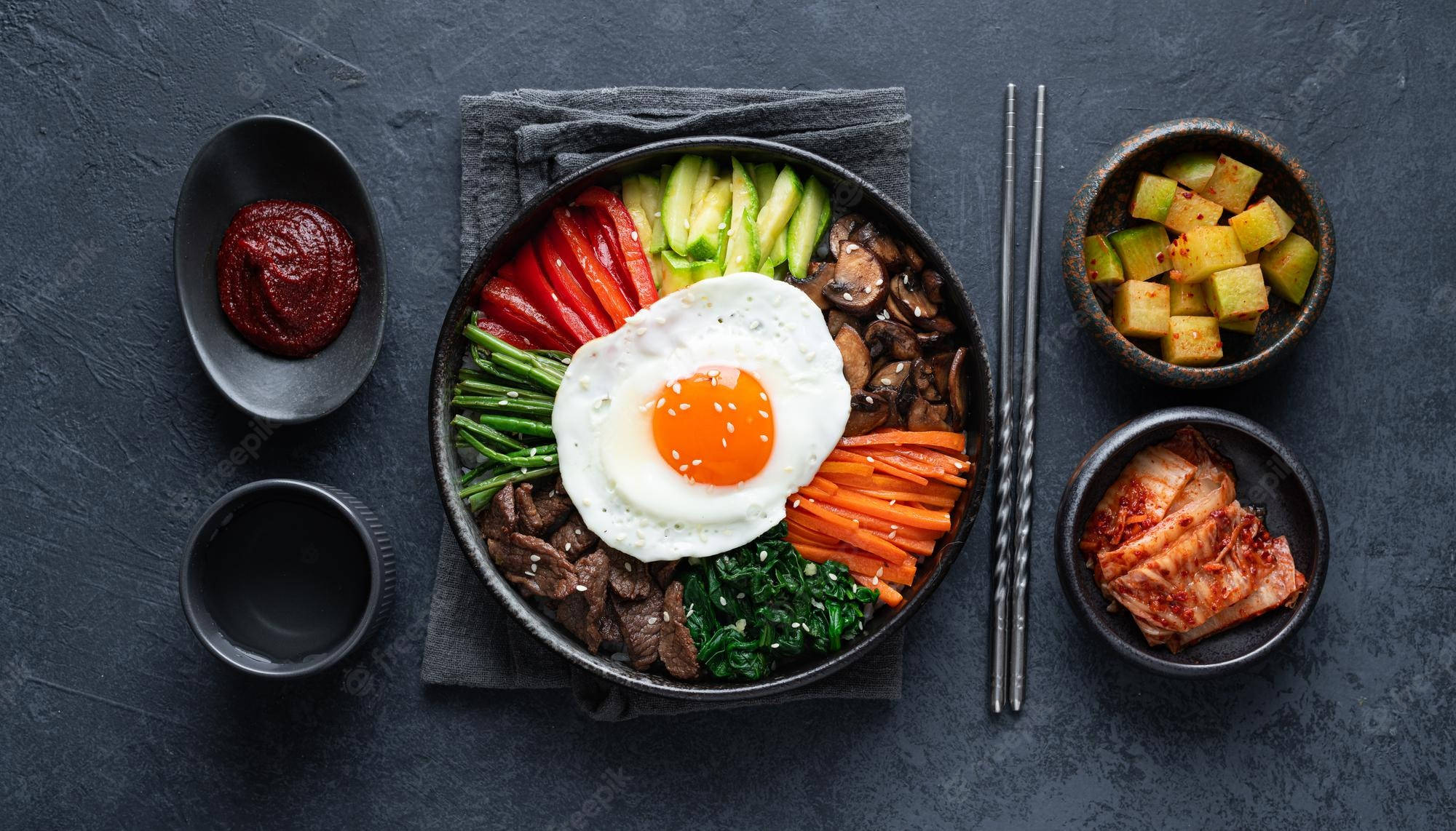 烹飪 桌布 壁紙 — 一個色彩繽紛的韓國石鍋拌飯，上面放著太陽蛋和各種蔬菜，置於深色石面上。