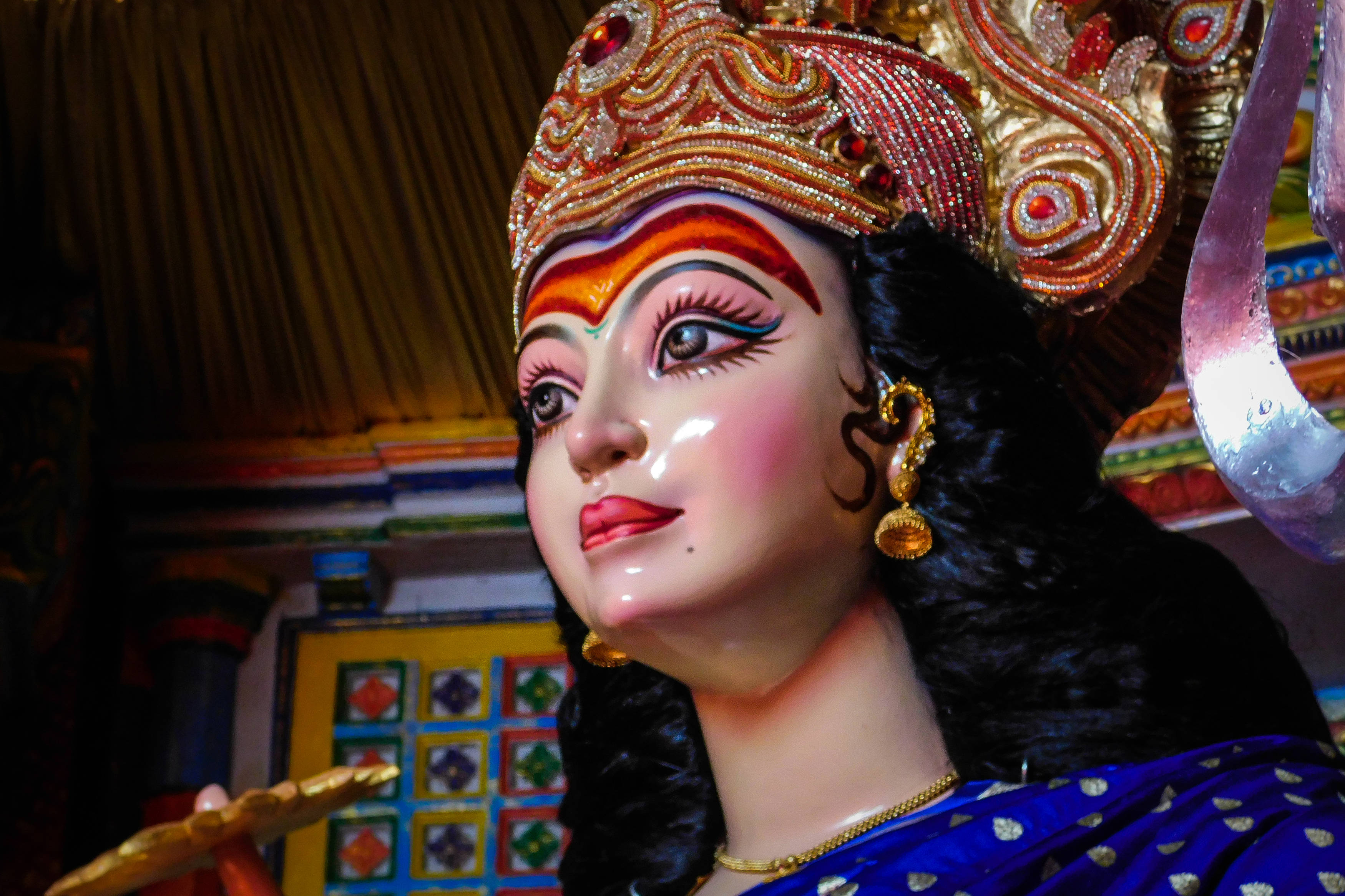 Navratri 桌布 壁紙 — 一個色彩鮮豔的印度教女神雕像特寫，飾有金色珠寶和紅橙色頭飾。