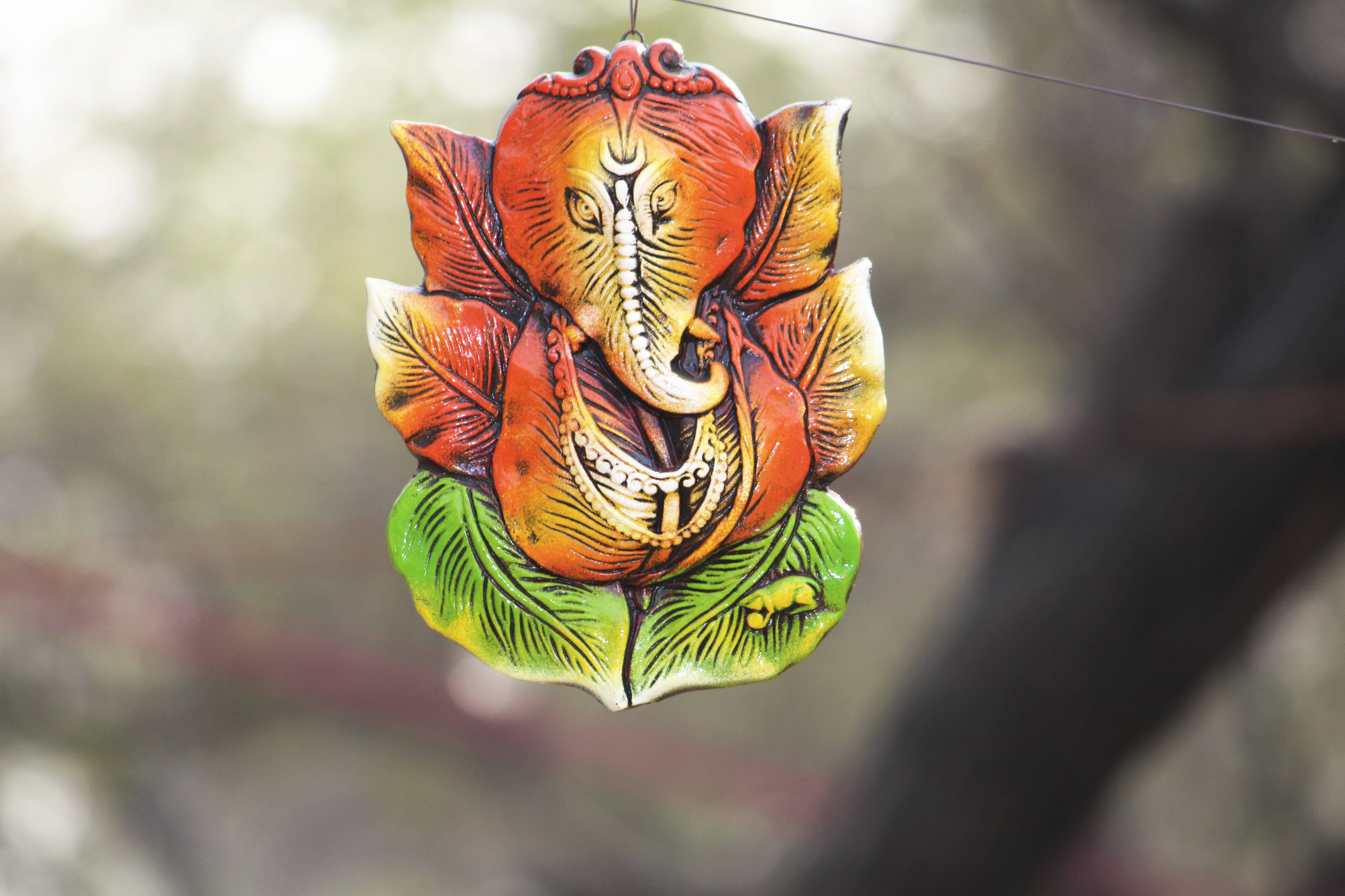 Ganesh 桌布 壁紙 — 一個色彩鮮豔的手繪象神雕像懸掛在柔和模糊的自然背景前。