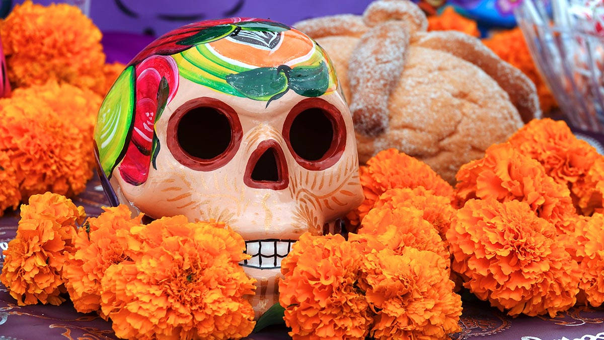 Mexican 桌布 壁紙 — 一個色彩鮮豔的糖骷髏，周圍環繞著橙色萬壽菊和甜麵包，作為亡靈節的中心裝飾。