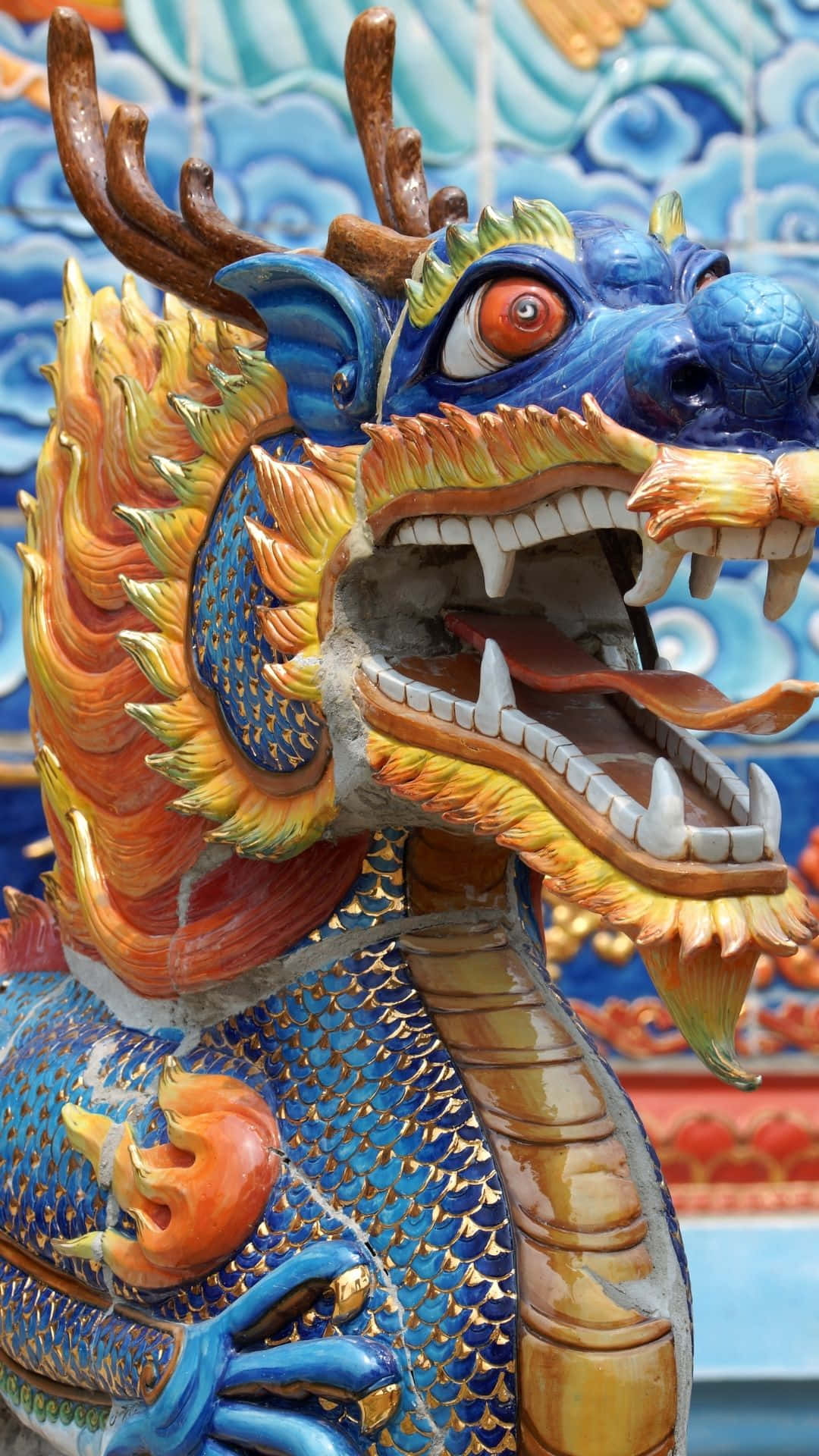 Blue Dragon 桌布 壁紙 — 一個色彩鮮豔的陶瓷龍雕塑，帶有藍色鱗片、橙色鬃毛和兇猛的紅色眼睛，背景是瓷磚。