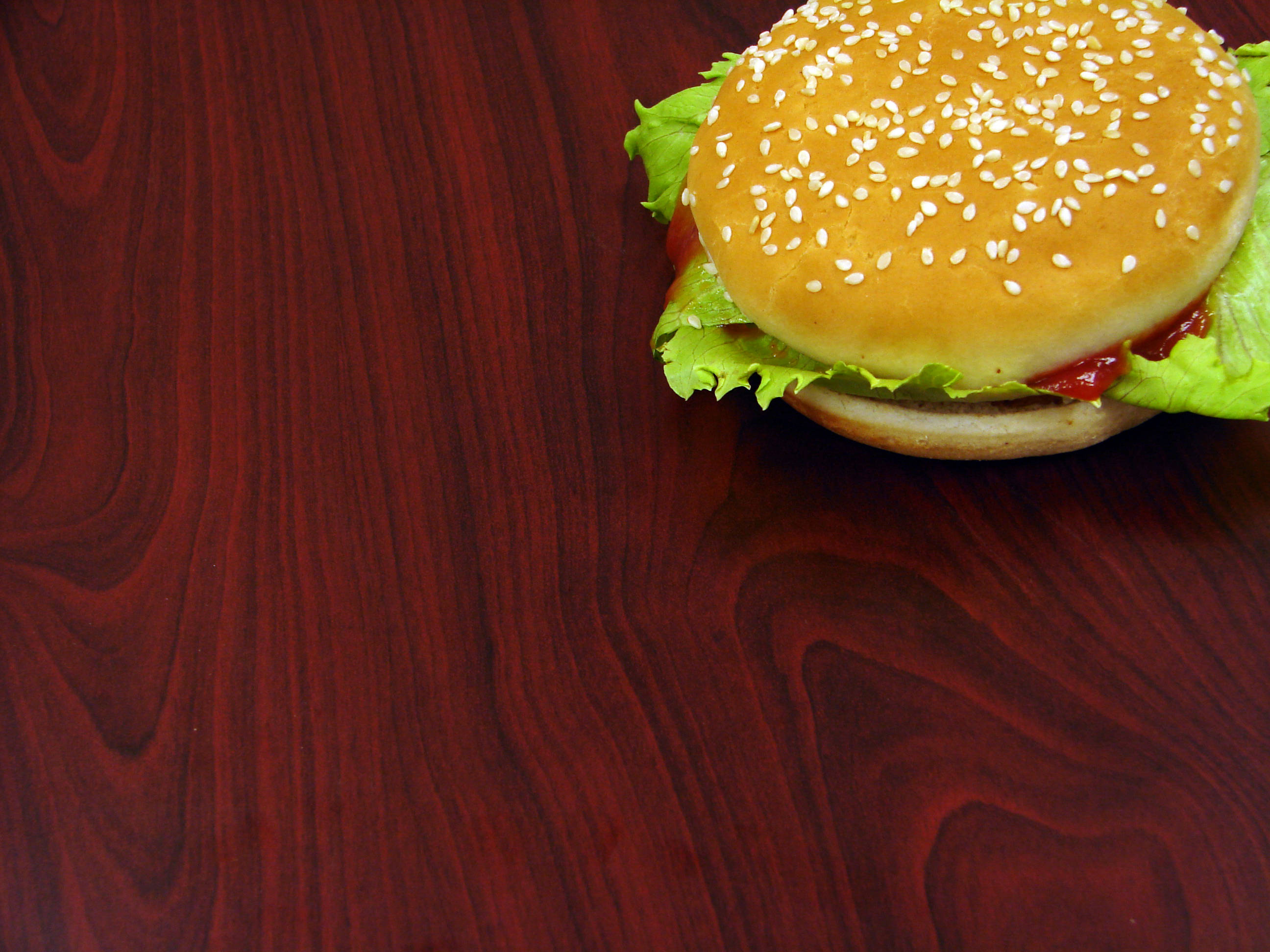 Burger 桌布 壁紙 — 一個芝麻籽漢堡配生菜和番茄醬，放在深色木質表面上。