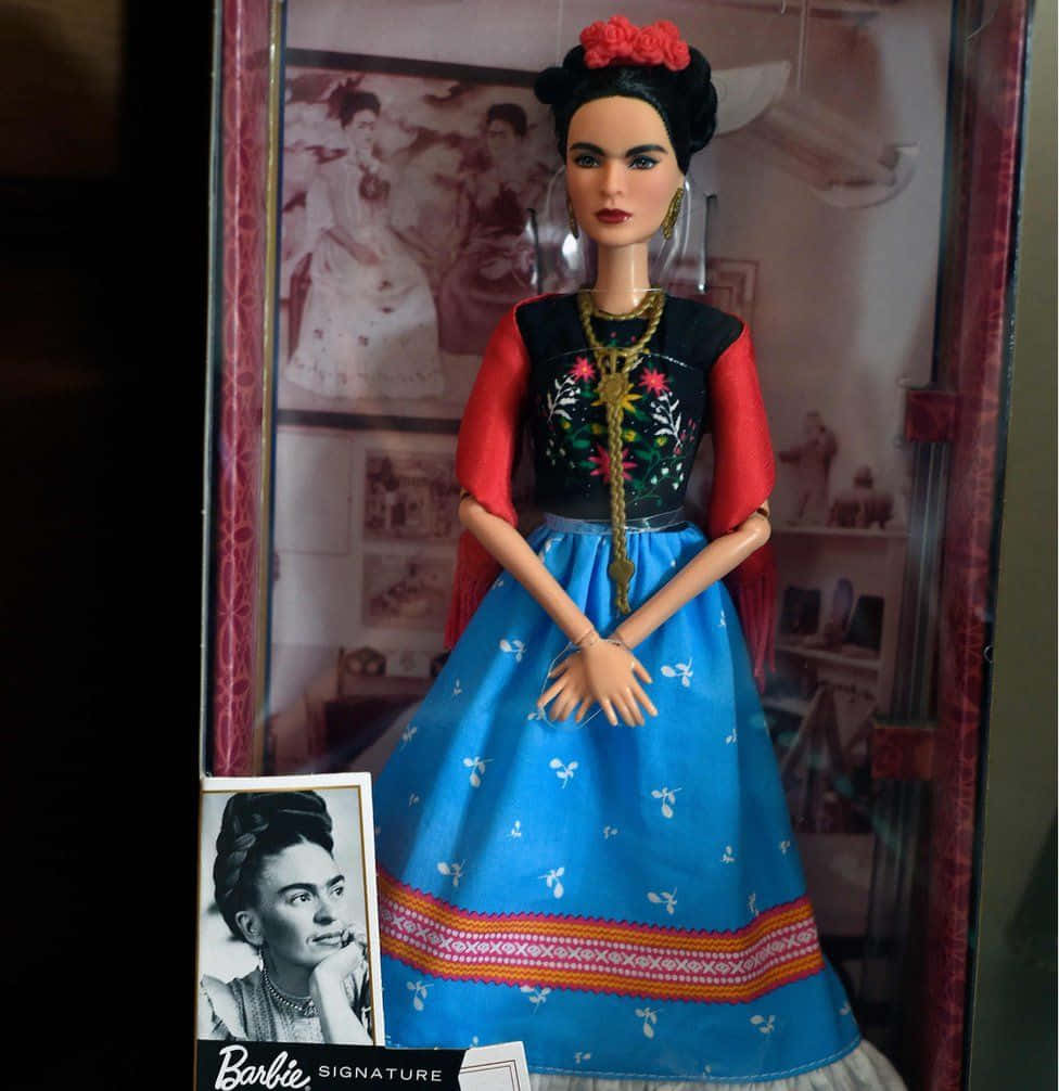 Barbie Doll 桌布 壁紙 — 一個芭比簽名系列娃娃，打扮成芙烈達·卡蘿，穿著鮮豔的藍色裙子、帶紅色袖子的刺繡黑色上衣和花卉頭飾。