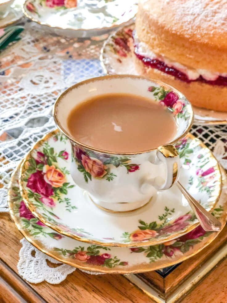 Teatime 桌布 壁紙 — 一個花卉圖案的茶杯盛滿茶，放在蕾絲杯墊上，旁邊有一個夾心果醬的千層蛋糕。