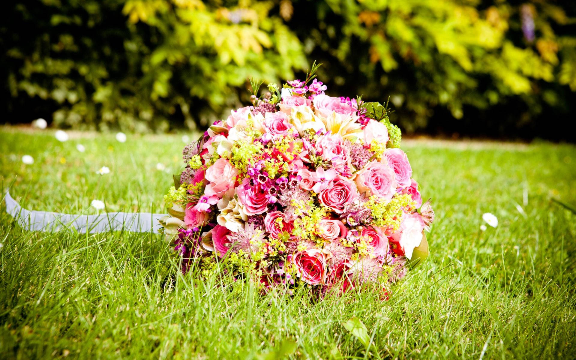 Wedding Aesthetic 桌布 壁紙 — 一個茂盛的粉紅色和綠色花束放在充滿活力的綠色草地上，背景是模糊的樹葉。