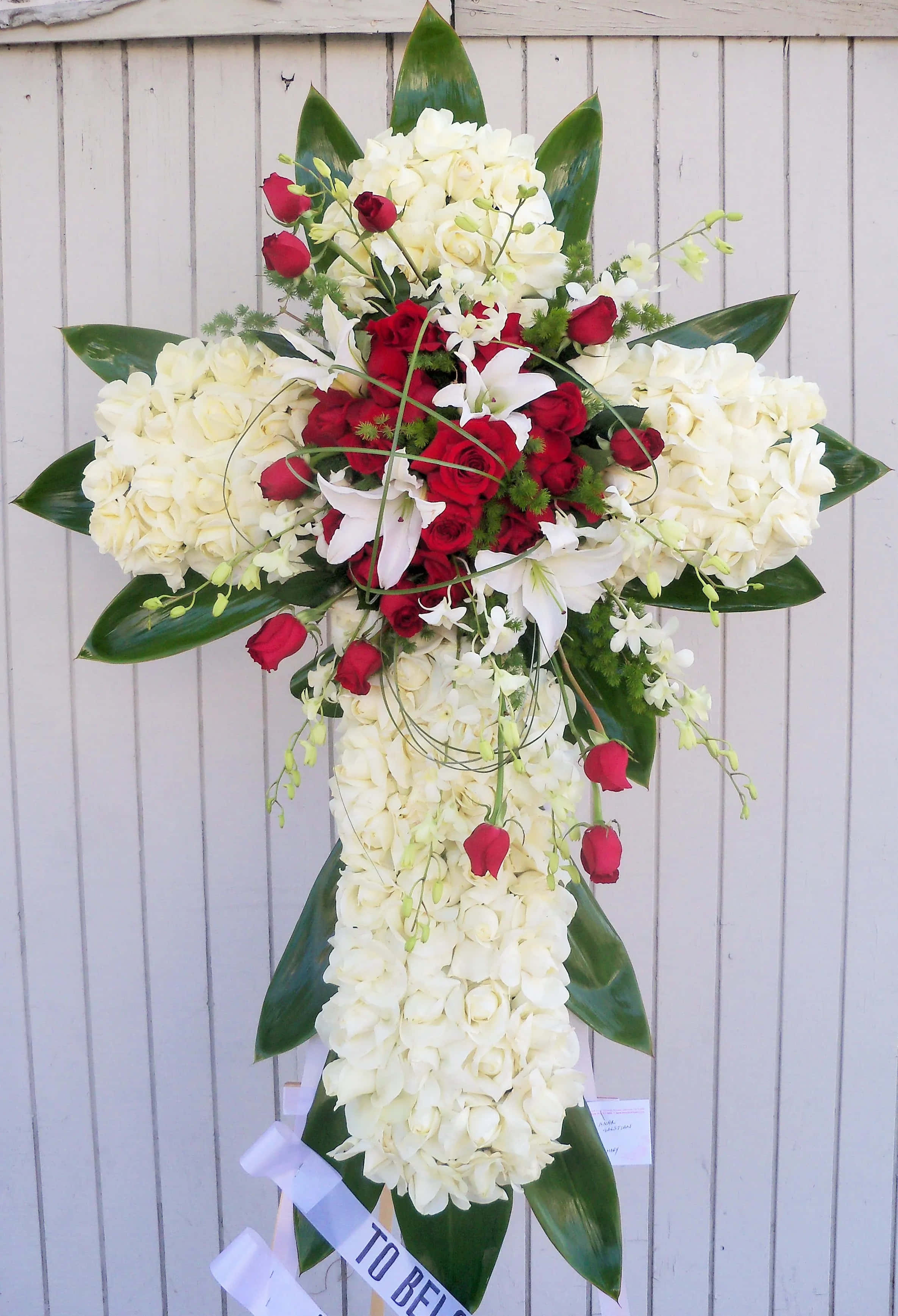 Funeral Flower Arrangements 桌布 壁紙 — 一個莊嚴的花卉十字架佈置，以白玫瑰、繡球花和紅玫瑰襯托淺色木柵欄。