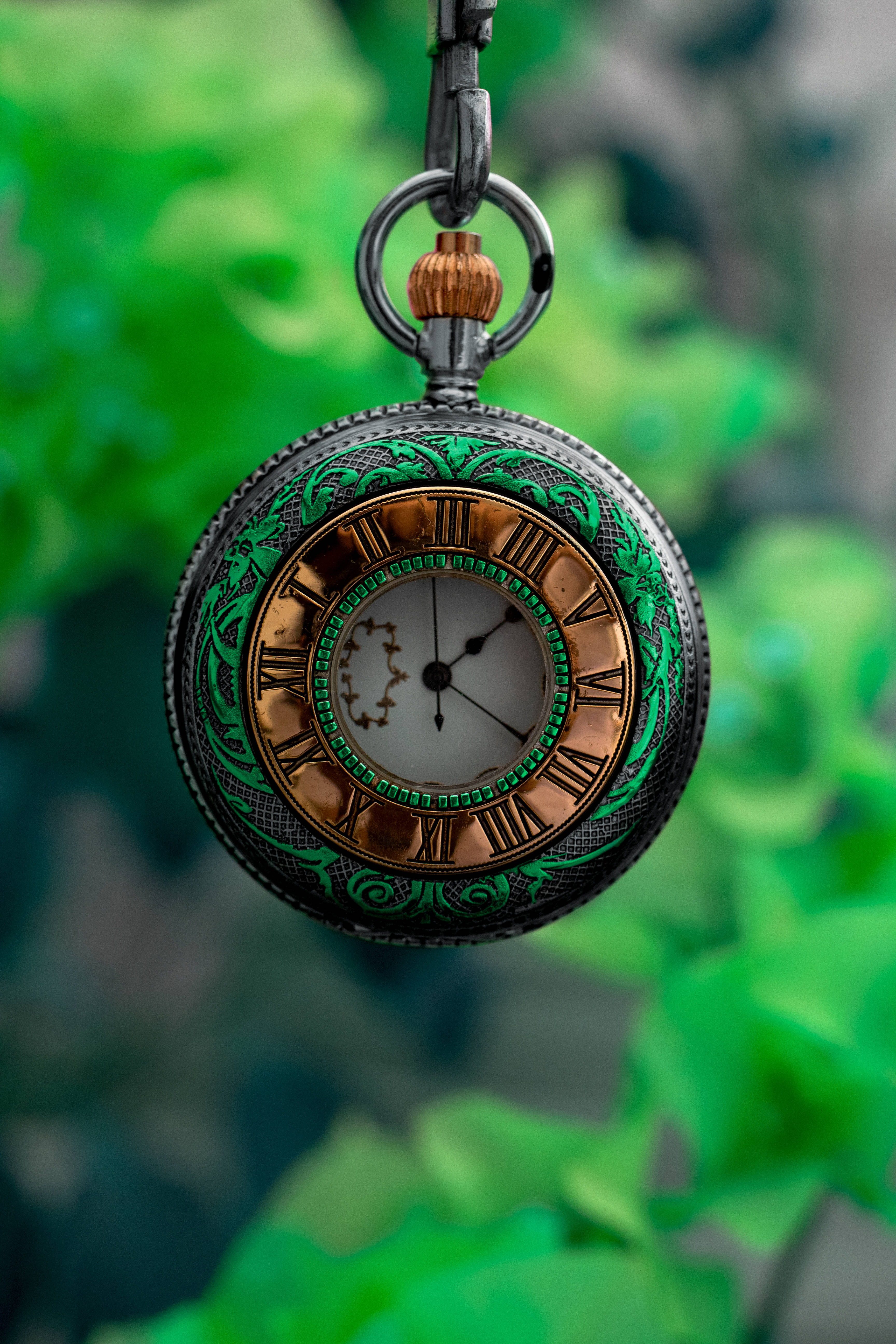 Clock 桌布 壁紙 — 一個華麗的復古懷錶，帶有綠色鏤空花紋和羅馬數字，懸掛在模糊的綠色樹葉背景前。