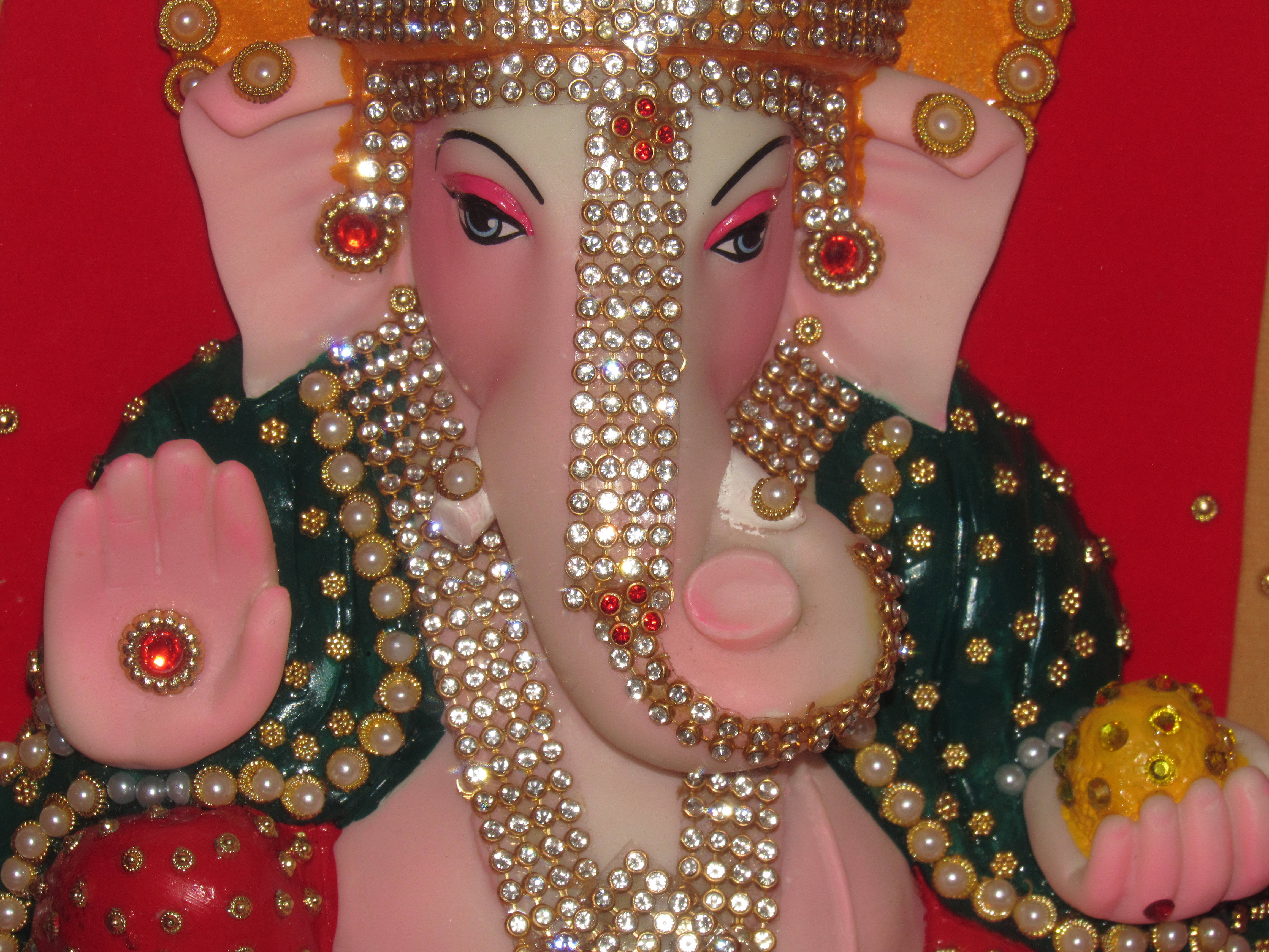 Ganesh 桌布 壁紙 — 一個華麗的象頭神雕像特寫，飾有金飾、珍珠和紅寶石，背景為鮮紅色。