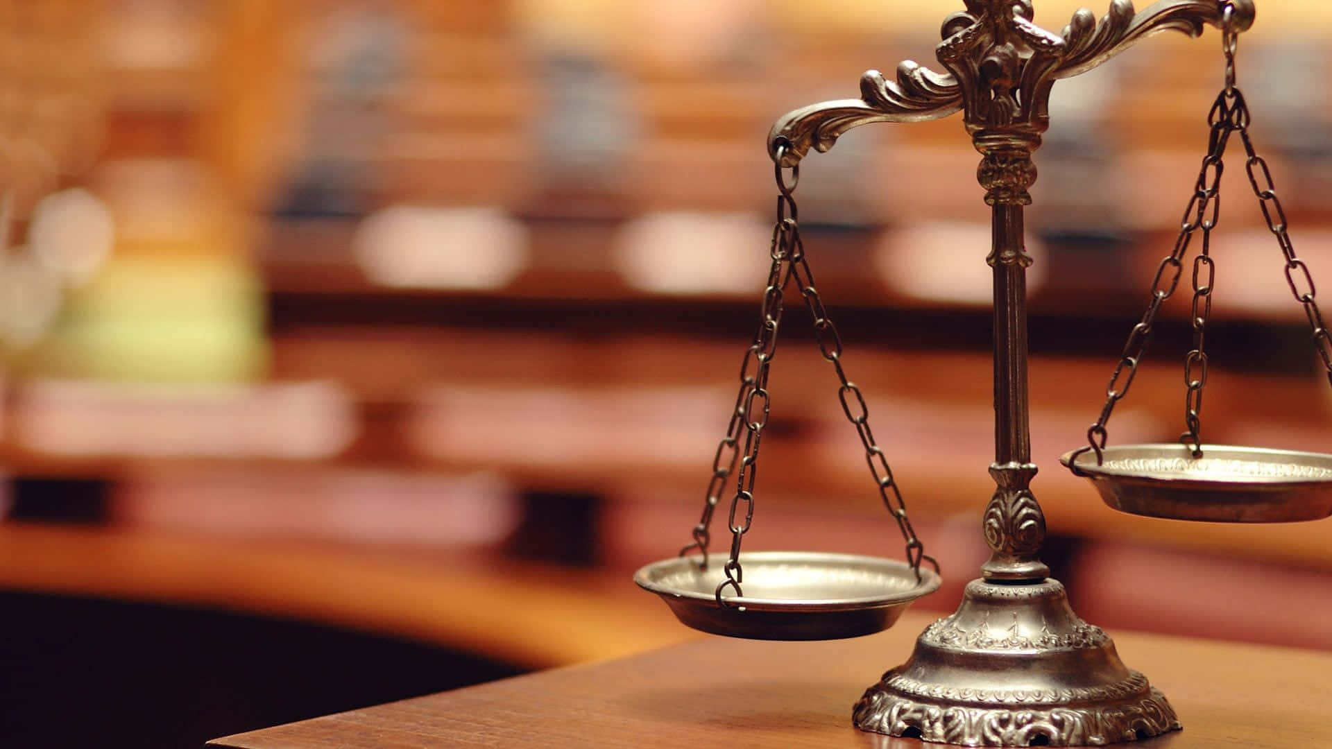 Courtroom 桌布 壁紙 — 一個華麗的金屬正義天秤平衡地放在一張木桌上，背景是溫暖照明的法庭，後面有模糊的書架。