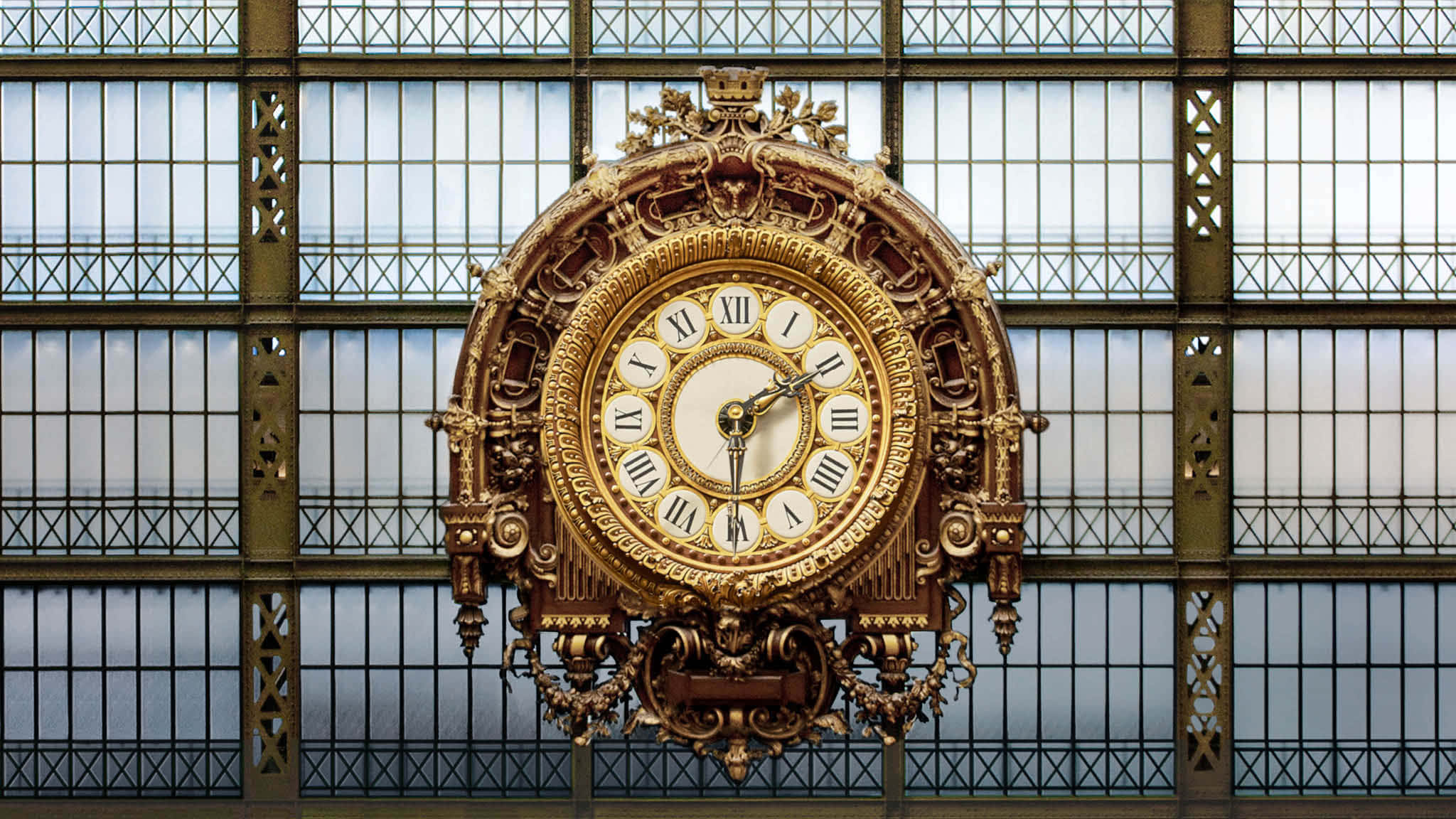 Clock 桌布 壁紙 — 一個華麗的金色時鐘帶有羅馬數字，懸掛在寬闊的玻璃和鐵製火車站天花板上。