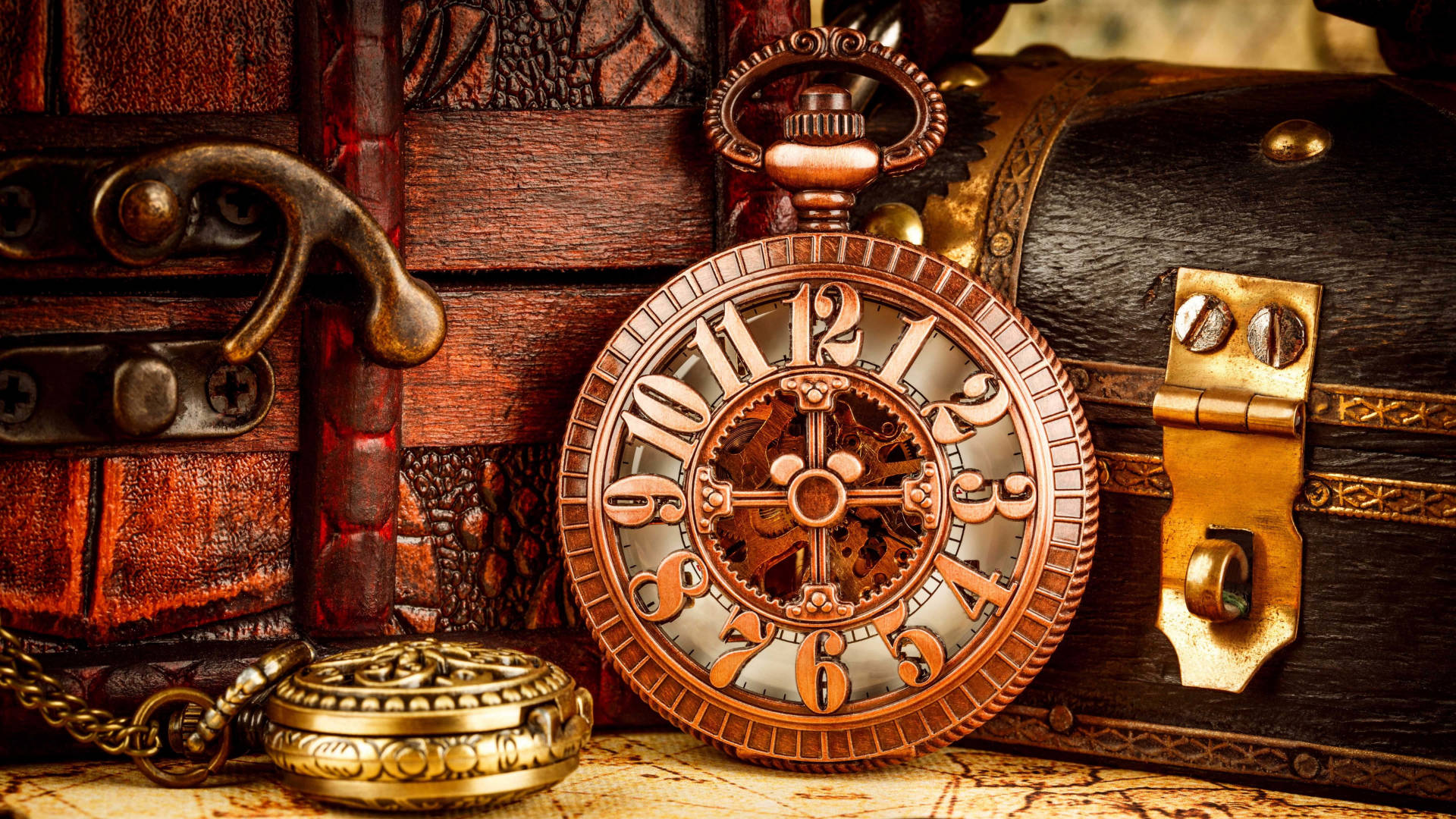 Clock 桌布 壁紙 — 一個華麗的銅製懷錶，帶有可見的齒輪，放在一張復古地圖上，旁邊是一個帶有黃銅配件的皮革包裹的寶箱。
