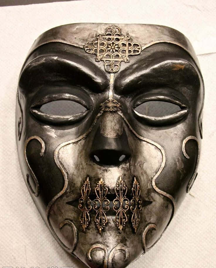 Death Eaters 桌布 壁紙 — 一個華麗的黑色和銀色劇院面具，額頭和嘴巴上有複雜的金色鏤空細節。