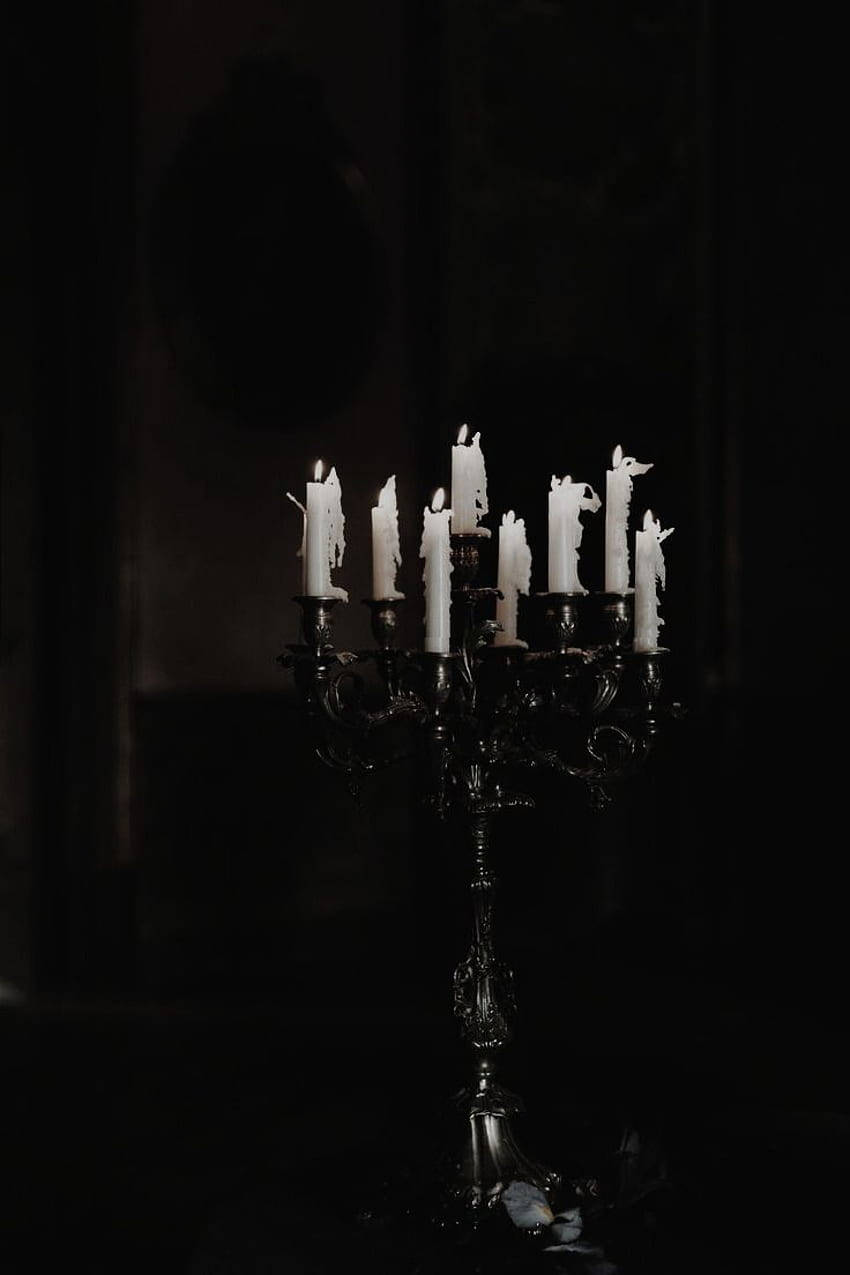 Goth Aesthetic 桌布 壁紙 — 一個華麗的黑色燭台，上面有閃爍的白色蠟燭，在黑暗神秘的房間中投射出柔和的光線。