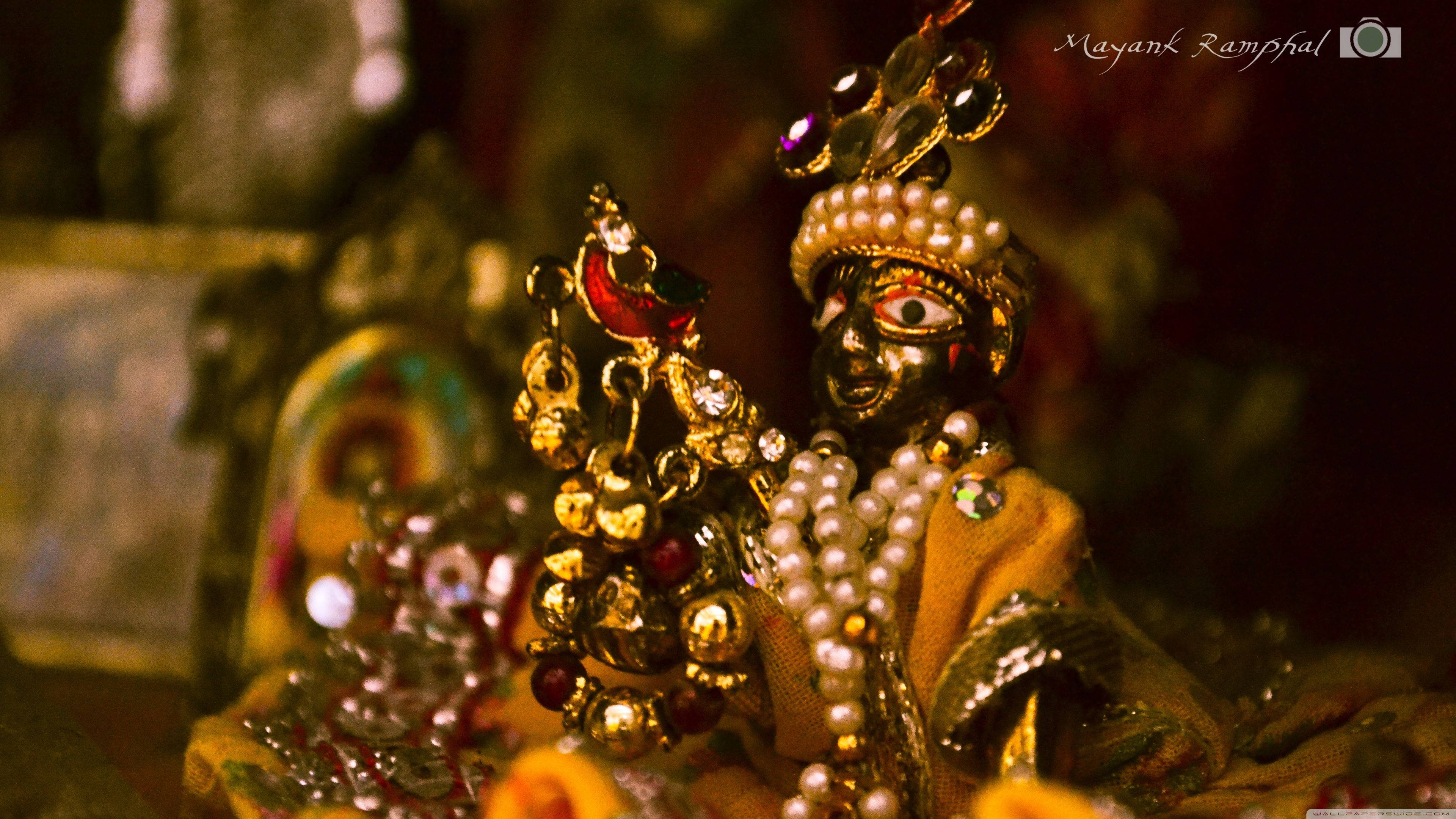 Hindu God 桌布 壁紙 — 一個華麗金色神像的特寫，飾有珍珠和寶石，在昏暗燈光下溫暖地發光。