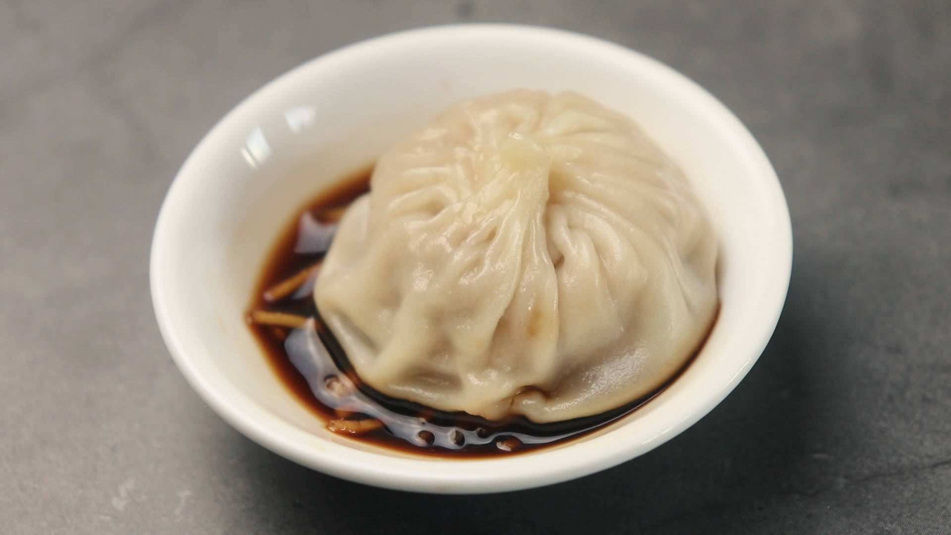 steam 桌布 壁紙 — 一個蒸餃放在灰色石面上的白色碗中，碗裡有深色醬油。