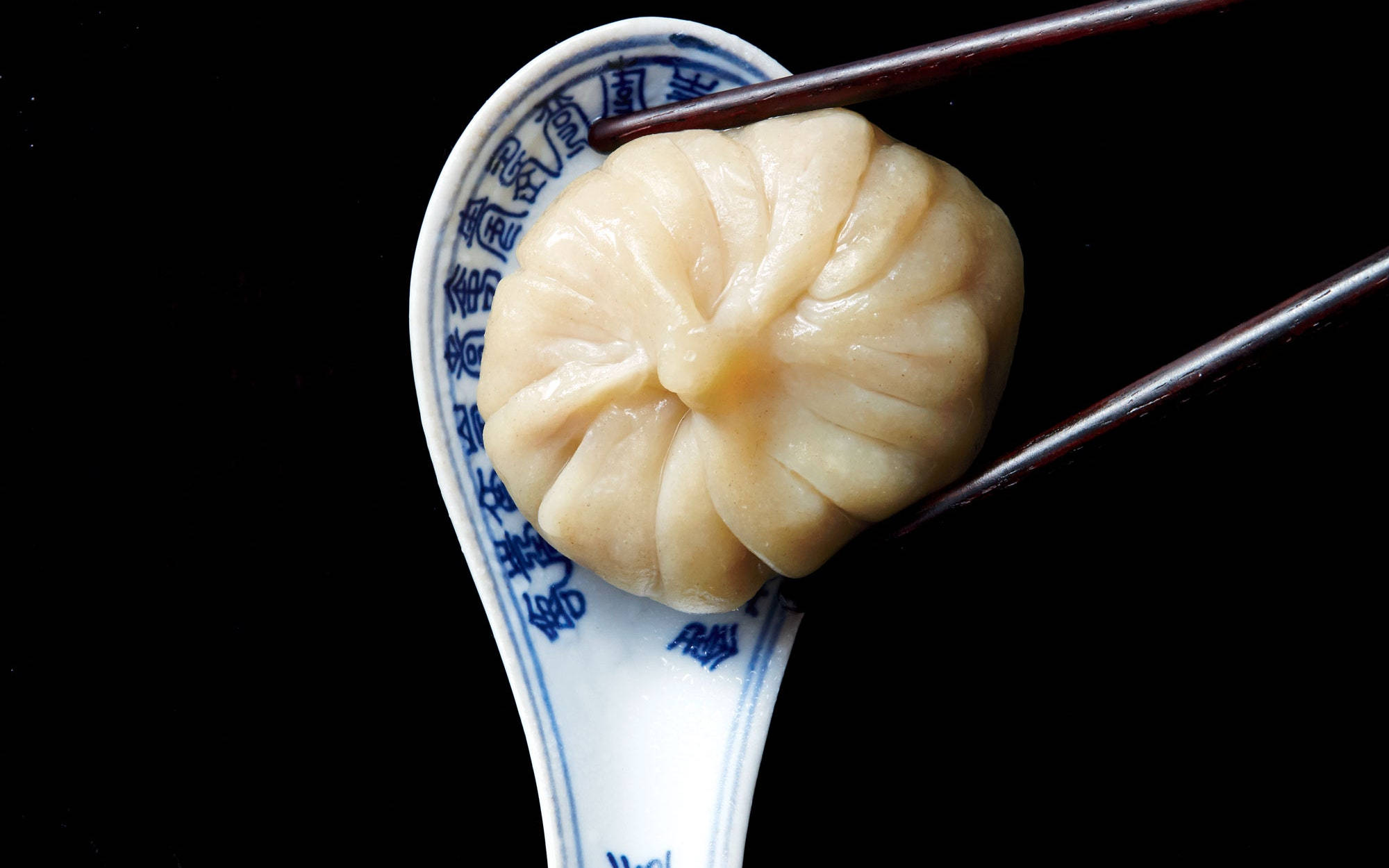 steam 桌布 壁紙 — 一個蒸餃被筷子夾著，放在藍白瓷湯匙上，背景為黑色。