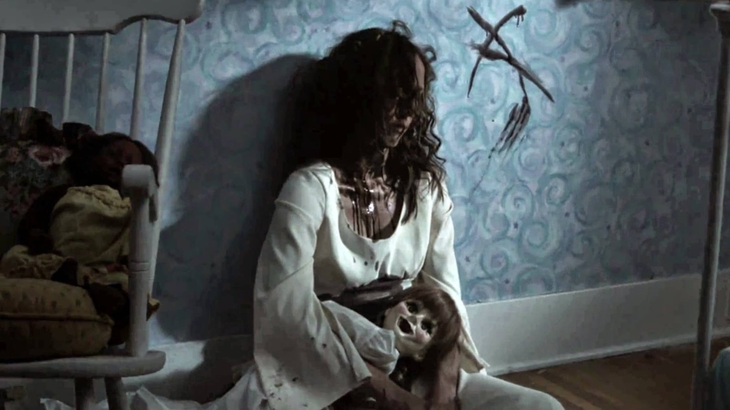 Annabelle 桌布 壁紙 — 一個蒼白的女人穿著沾污的白色連衣裙，抱著一個張大嘴巴的娃娃，背景是旋轉的藍色壁紙。