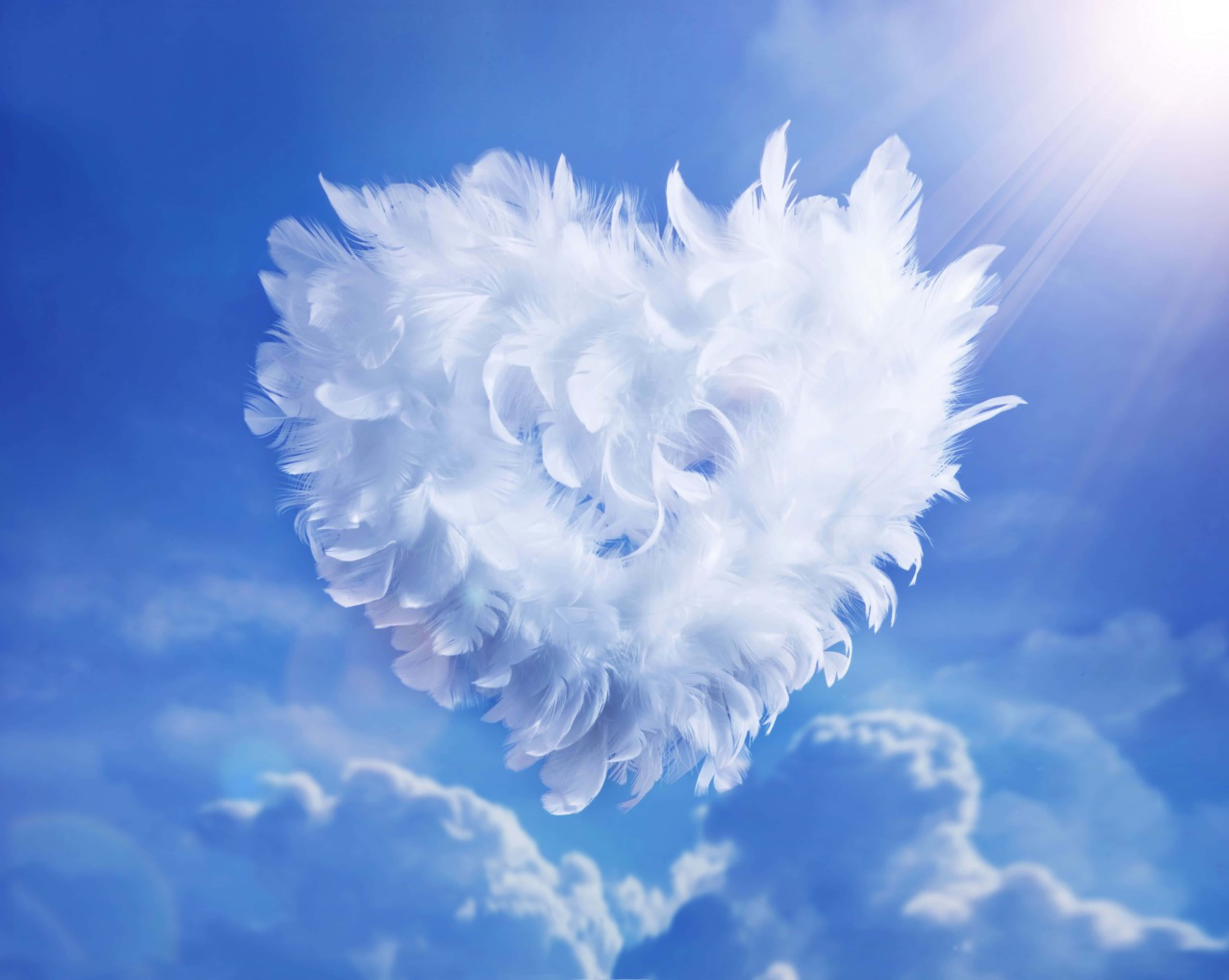 White Heart 桌布 壁紙 — 一個蓬鬆的白色羽毛心形在明亮的藍天中寧靜地漂浮，伴隨著陽光和柔軟的雲朵。