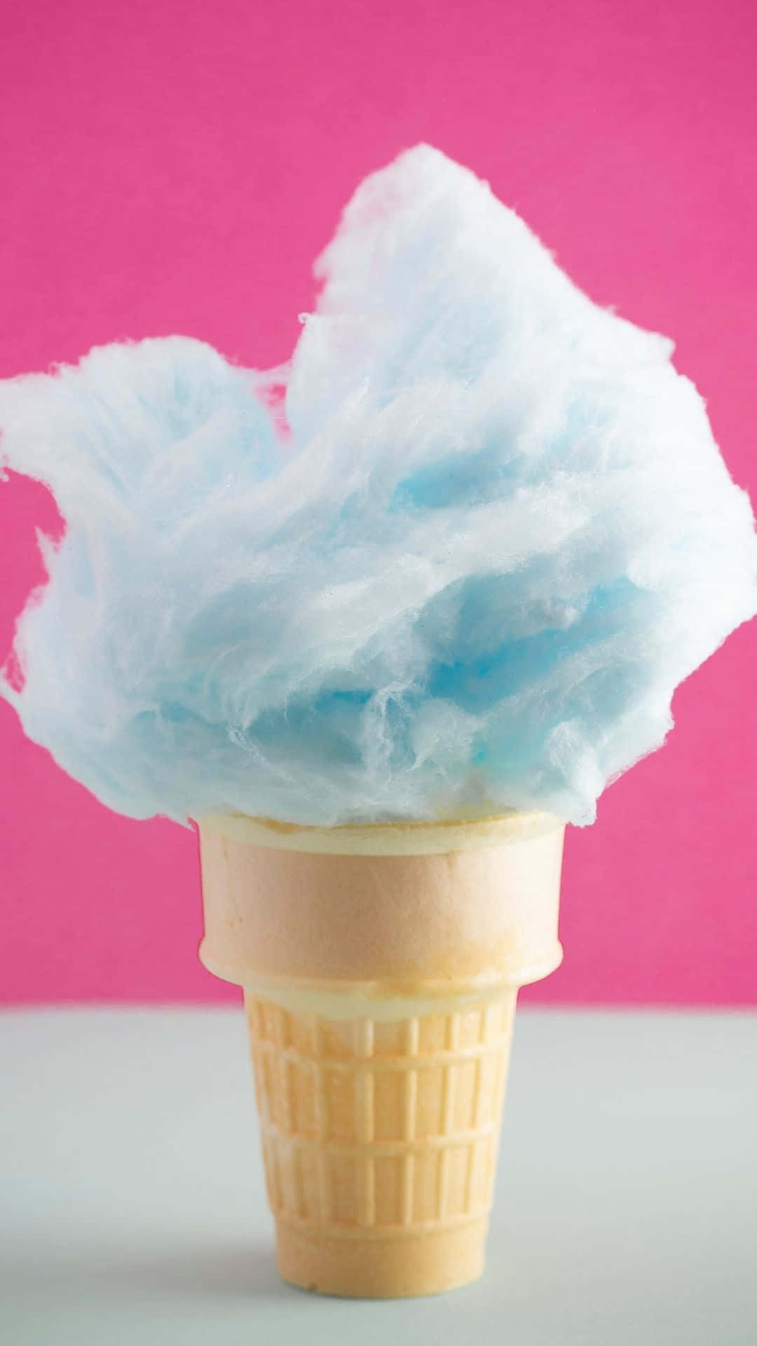 Cotton Candy 桌布 壁紙 — 一個蓬鬆的藍色棉花糖從鬆餅筒中溢出，襯托著充滿活力的粉紅色背景。
