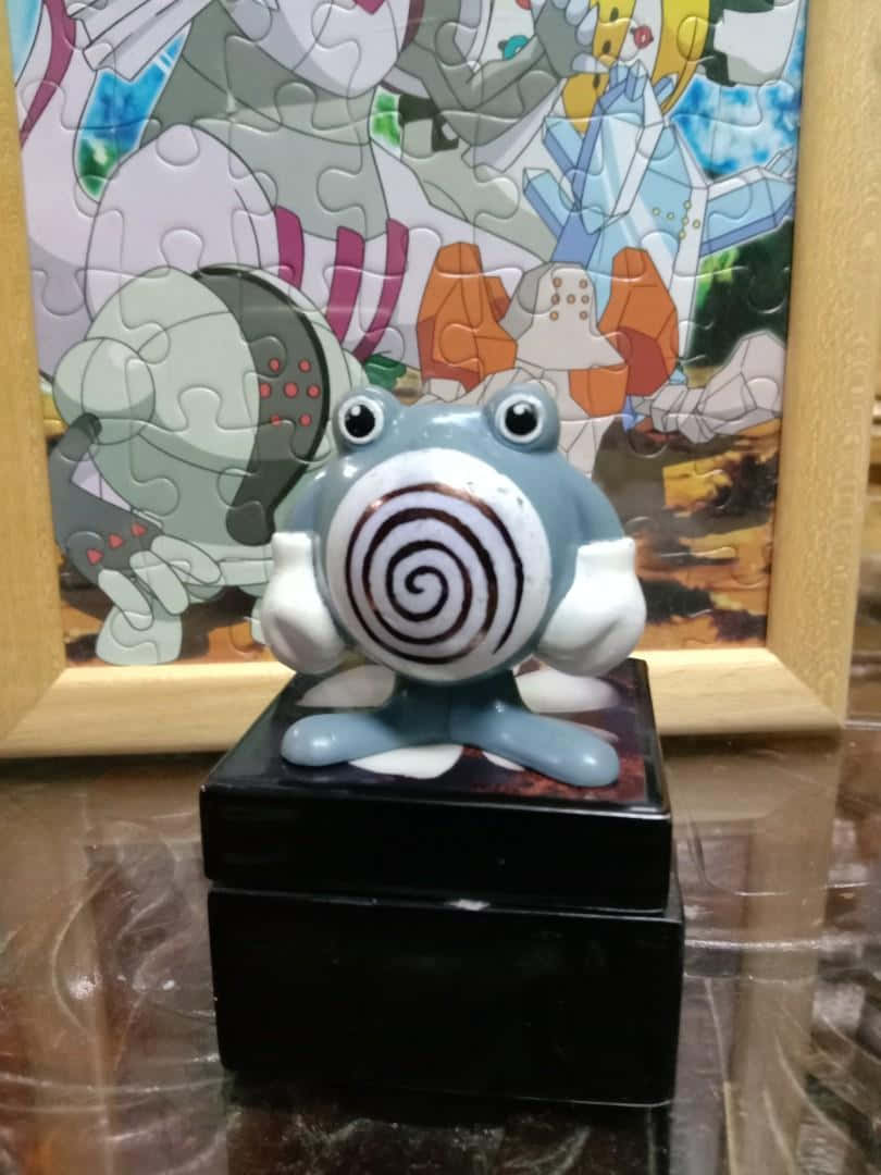 Pokémon 手機 桌布 壁紙 — 一個藍白相間、螺旋臉的動漫青蛙公仔坐在黑色底座上，前面是一個裱框的拼圖，描繪了其他動漫角色。