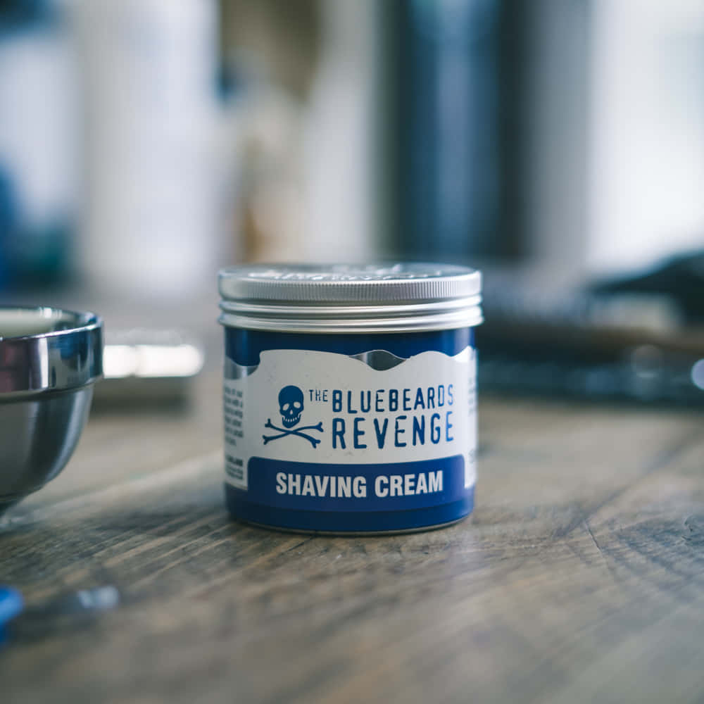 Shaving Cream 桌布 壁紙 — 一個藍白相間的「The Bluebeards Revenge」刮鬍膏罐放在木質表面上，旁邊有一個模糊的金屬碗。