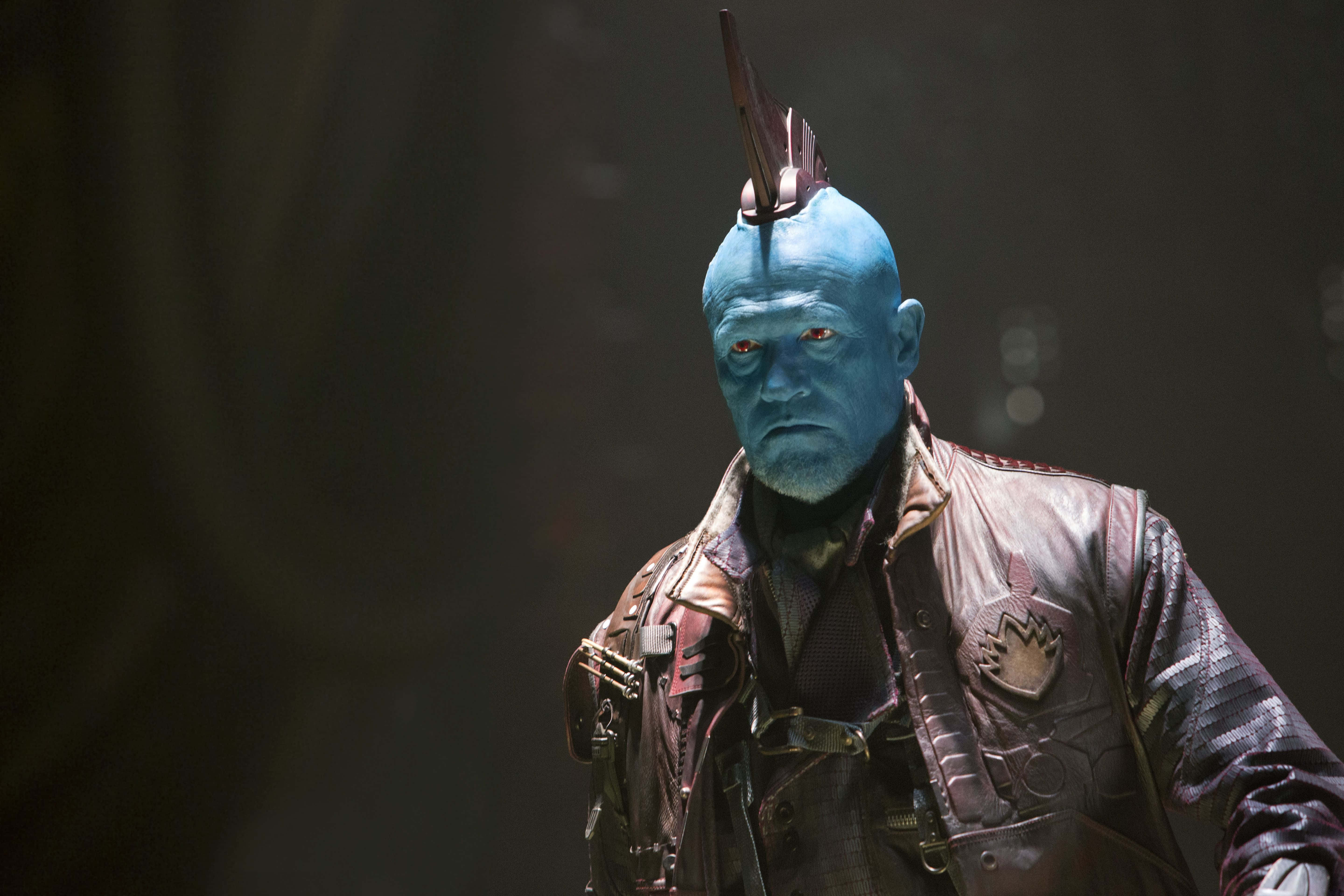 Yondu 桌布 壁紙 — 一個藍皮膚外星人，有著發光的紅眼睛和莫霍克髮型，站在昏暗的空間裡，穿著一件細節豐富的皮夾克。