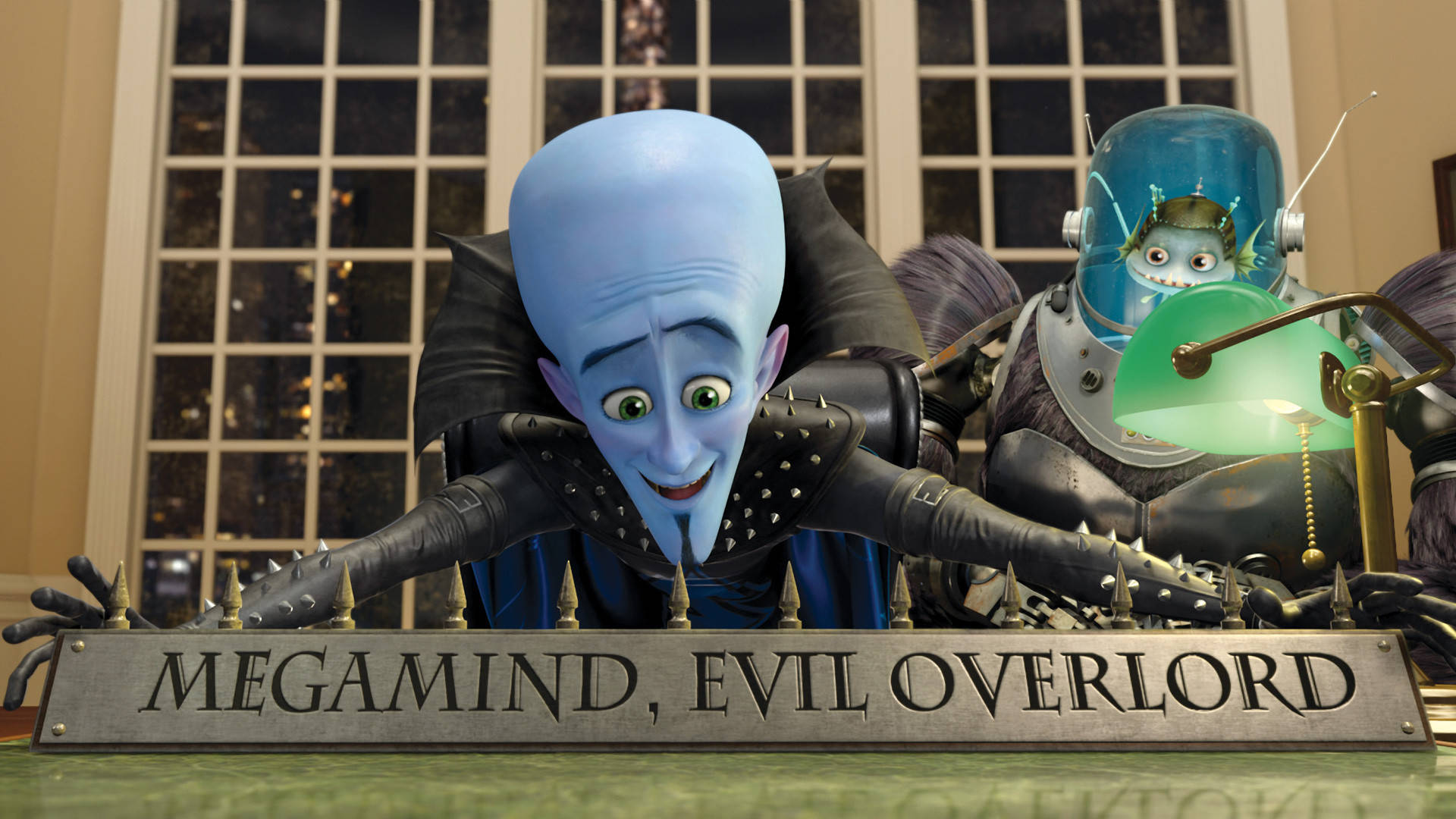 Cartoon 桌布 壁紙 — 一個藍皮膚的動畫反派咧嘴笑著，俯身在一張標有「MEGAMIND EVIL OVERLORD」的桌子上，旁邊是一個綠色燈光下的機器人。
